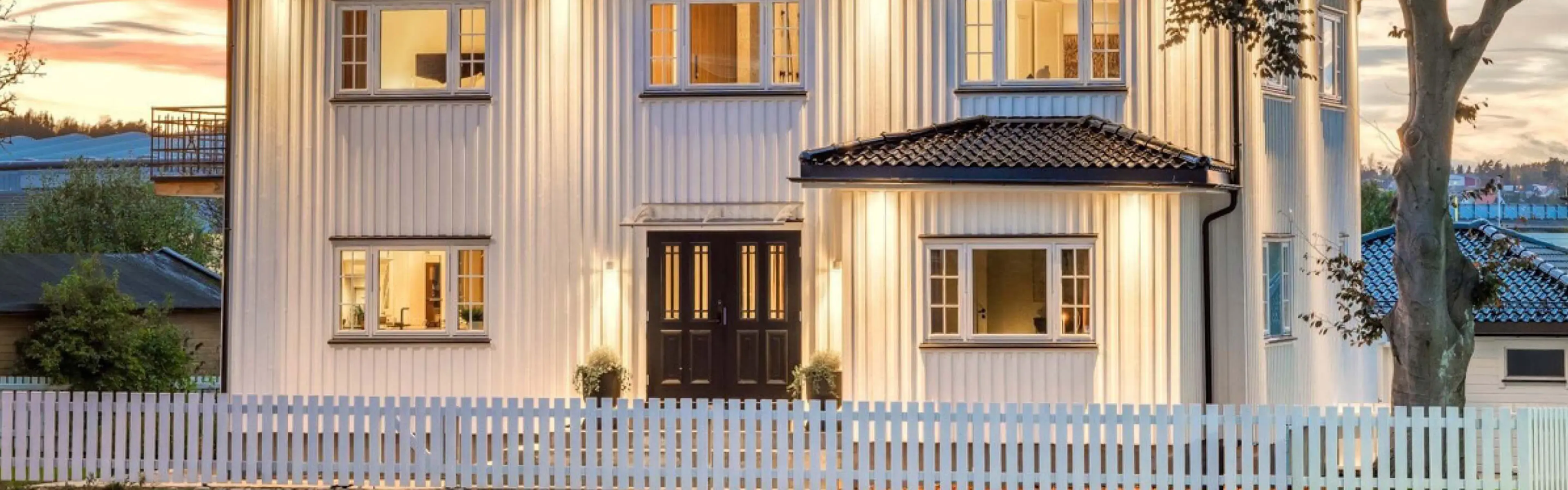 Hvitt hus med stakittgjerde og klassisk dobbel ytterdør i sort med profil og glass med sprosser.