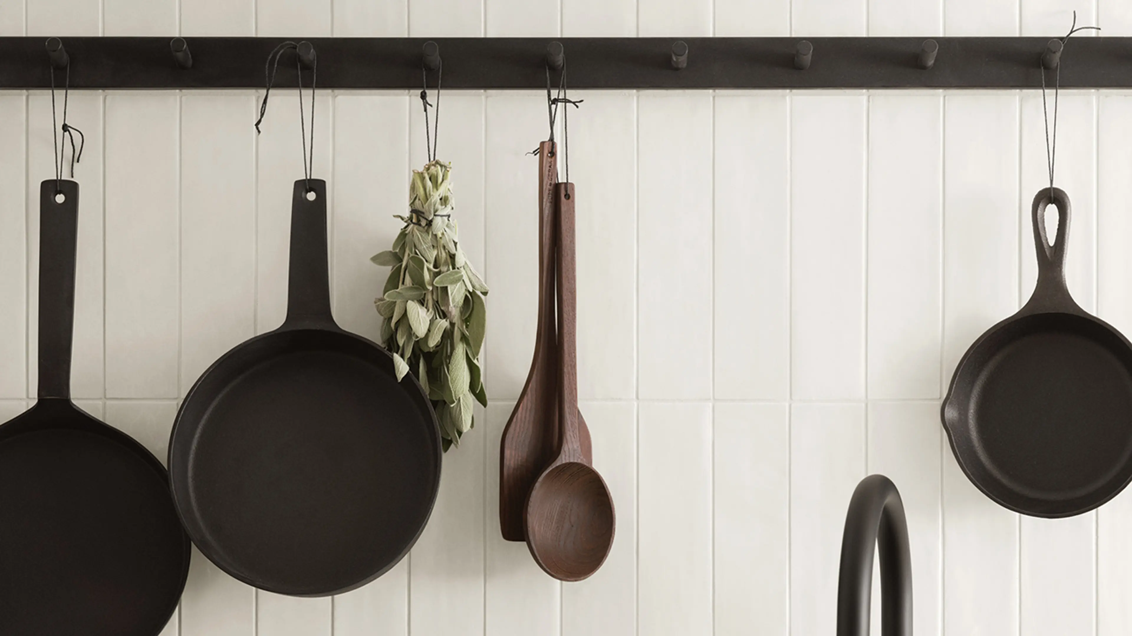 Svart knaggrekke med jernstekepanner hengende i landlig kjøkken.