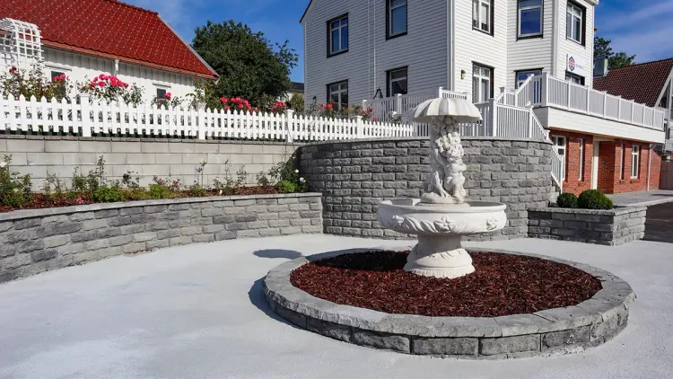 Gårdsplass med belegningsstein, betongtrapp og støttemur.