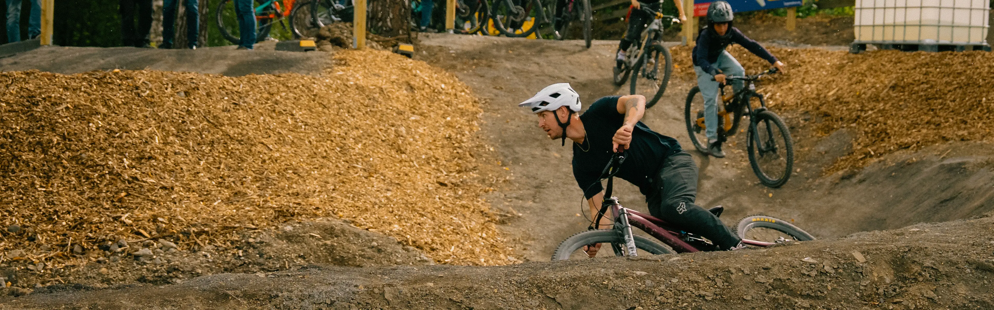 Flere gutter som sykler i sykkelpark mens det står folk å ser på.