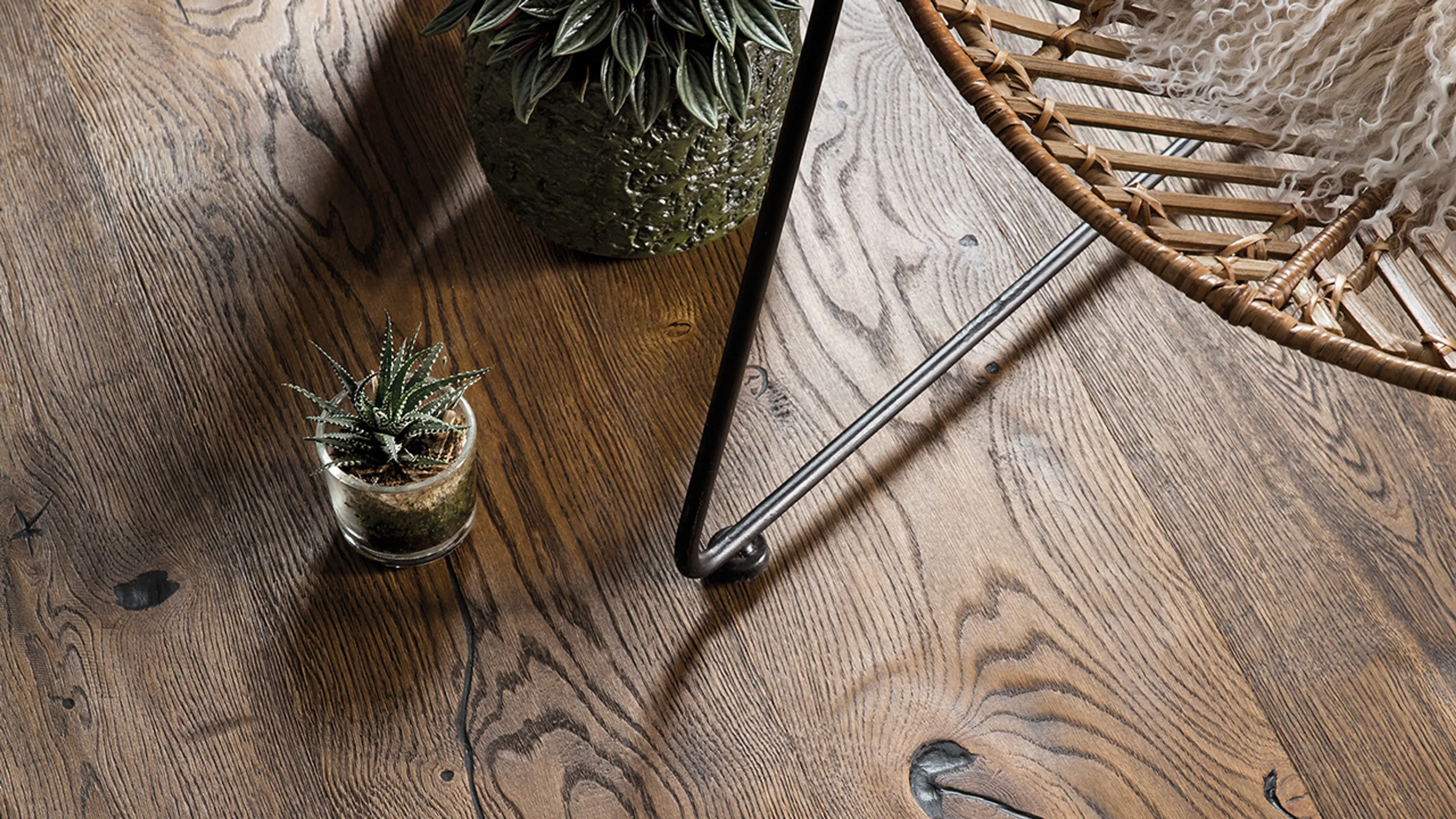 Nærbilde sett ovenfra av rustikt mørkt gulv i stue med planter.
