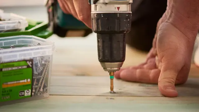 Nærbilde av drill som skrur inn syrefaste terrasseskruer i terrassebord.