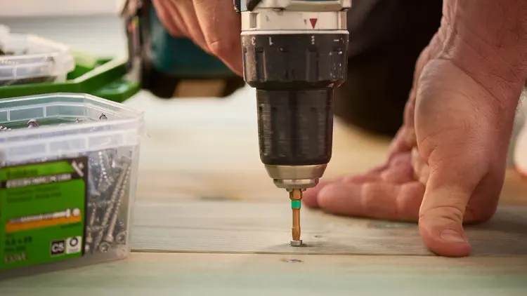Nærbilde av drill som skrur inn syrefaste terrasseskruer i terrassebord.