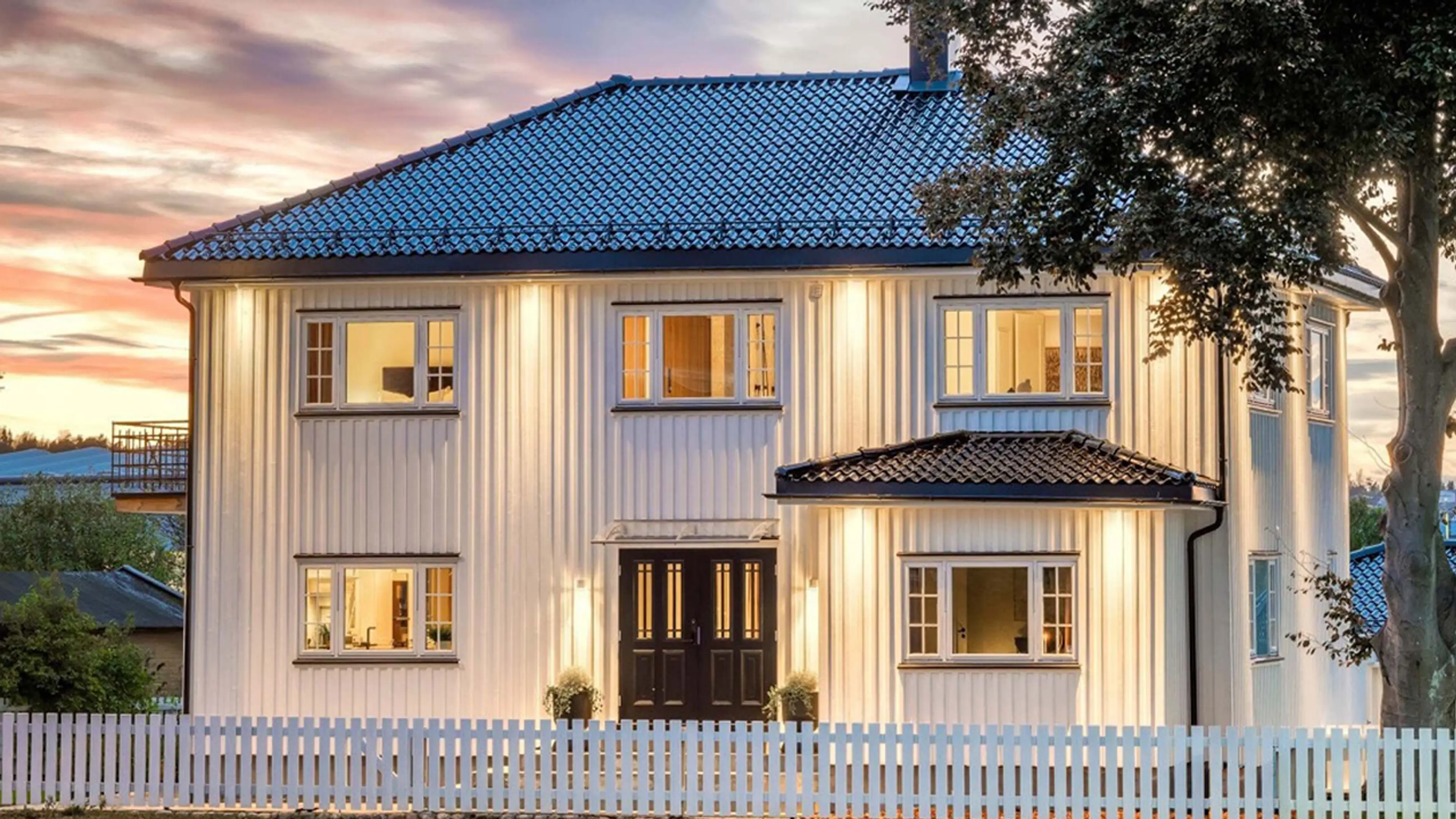 Hvitt hus med stakittgjerde og klassisk dobbel ytterdør i sort med profil og glass med sprosser.