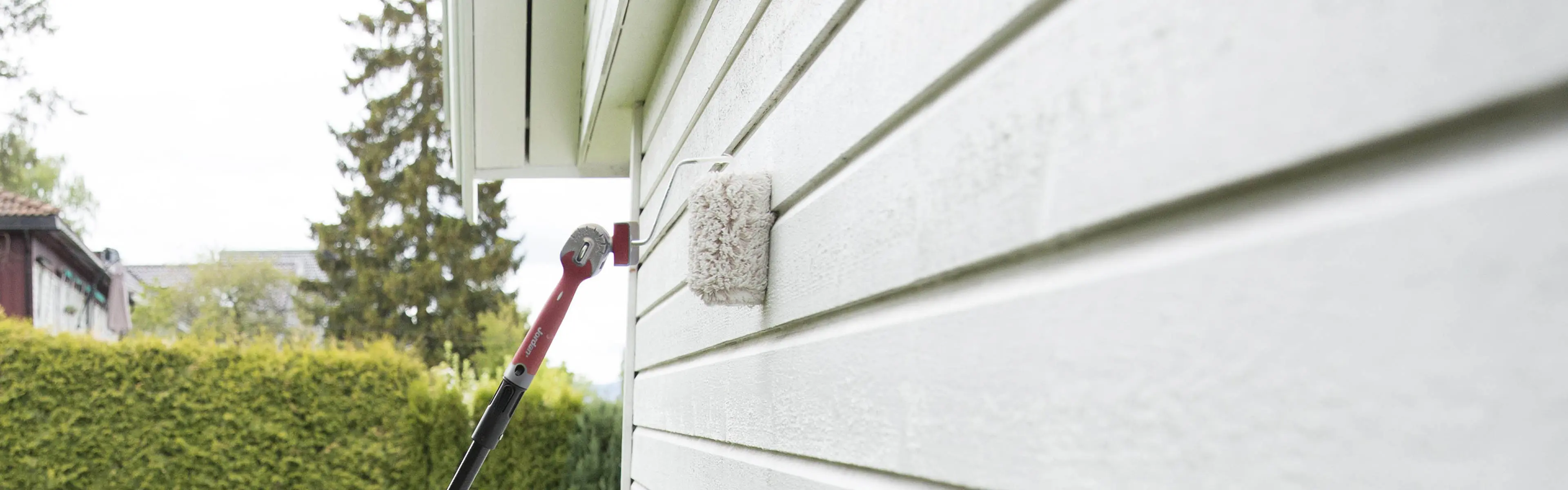 Nærbilde av male hus ute med malerulle og forlengerskaft.