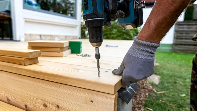 Snekker skrur inn skruer med drill i en terrasse som han bygger,