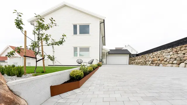 Multiblokk heller og mur i stein i oppkjørsel til hvitt hus.