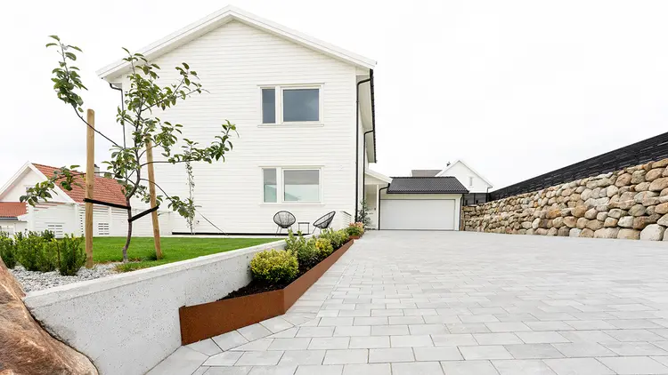 Multiblokk heller og mur i stein i oppkjørsel til hvitt hus.