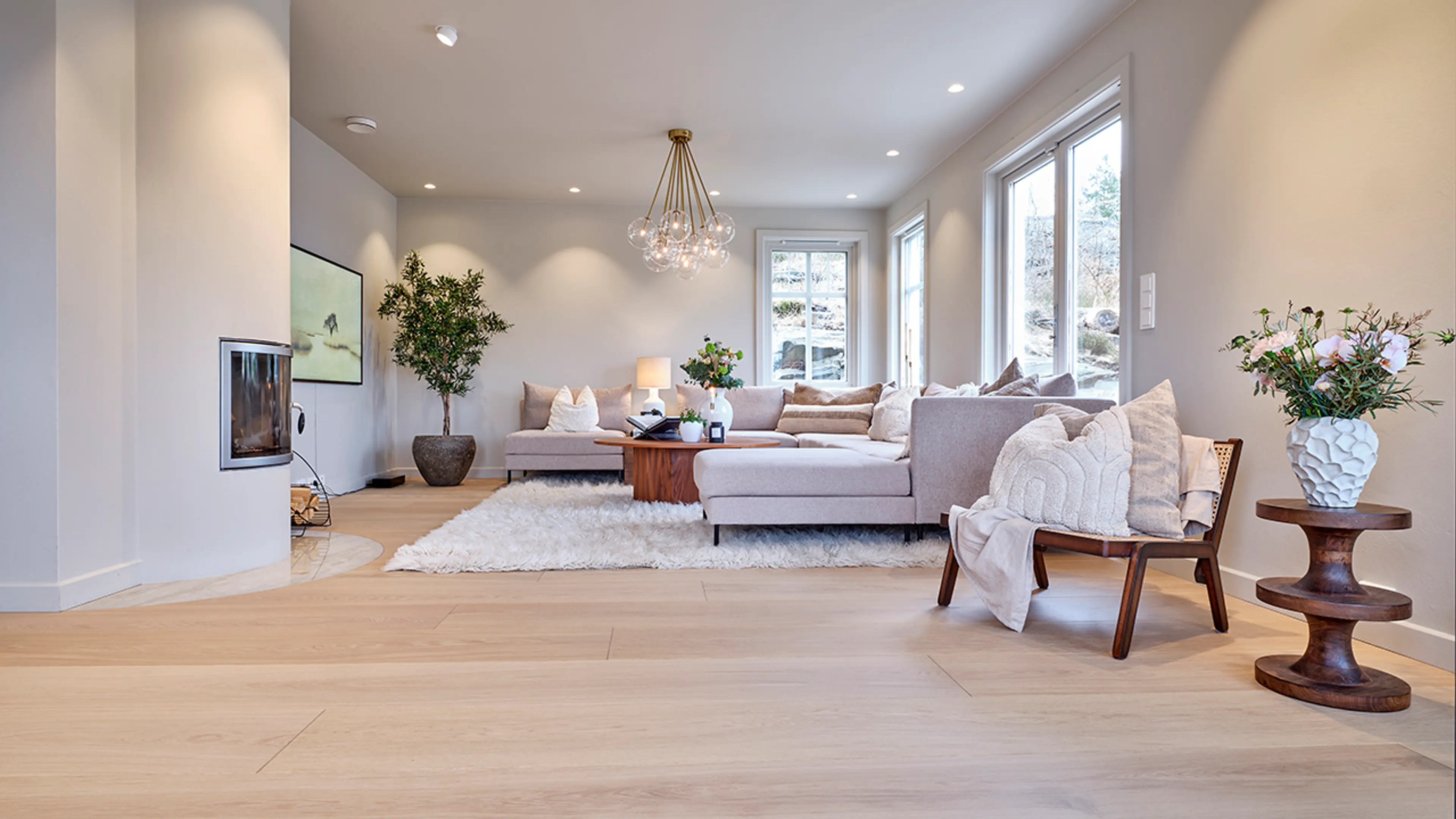 Greige stue med store sofa, bord i mørkt treverk og lyse gulv i eik.