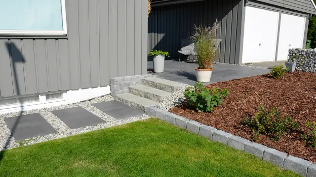 Hagesti med trapp langs husvegg som illustrerer legge steinheller i hagen.