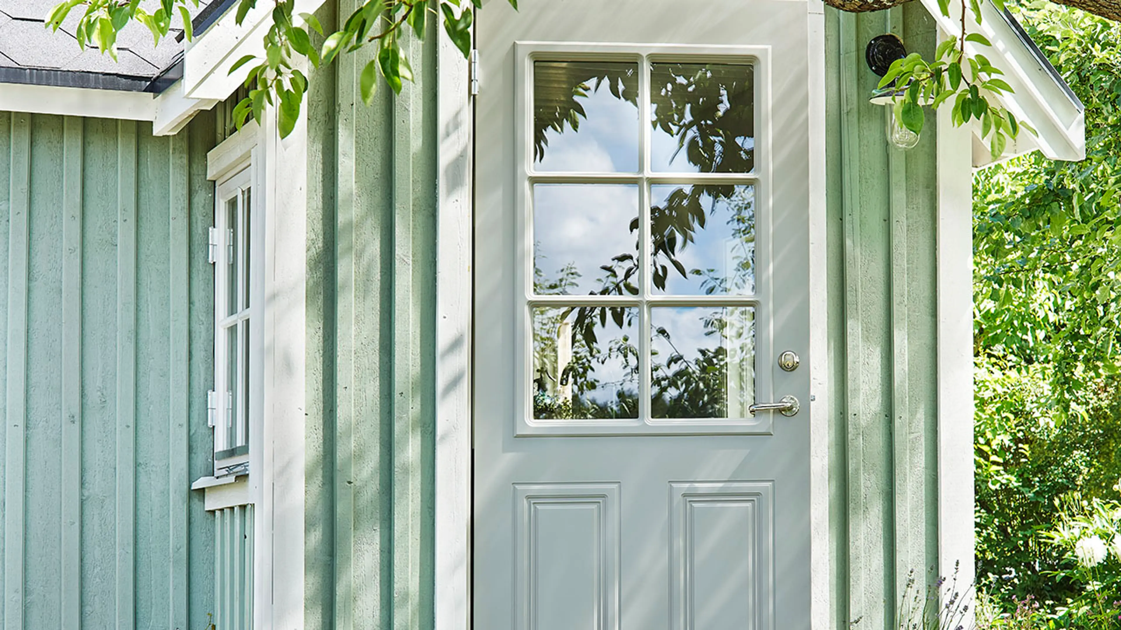 Lysegrå klassisk ytterdør på lysegrønt hus.