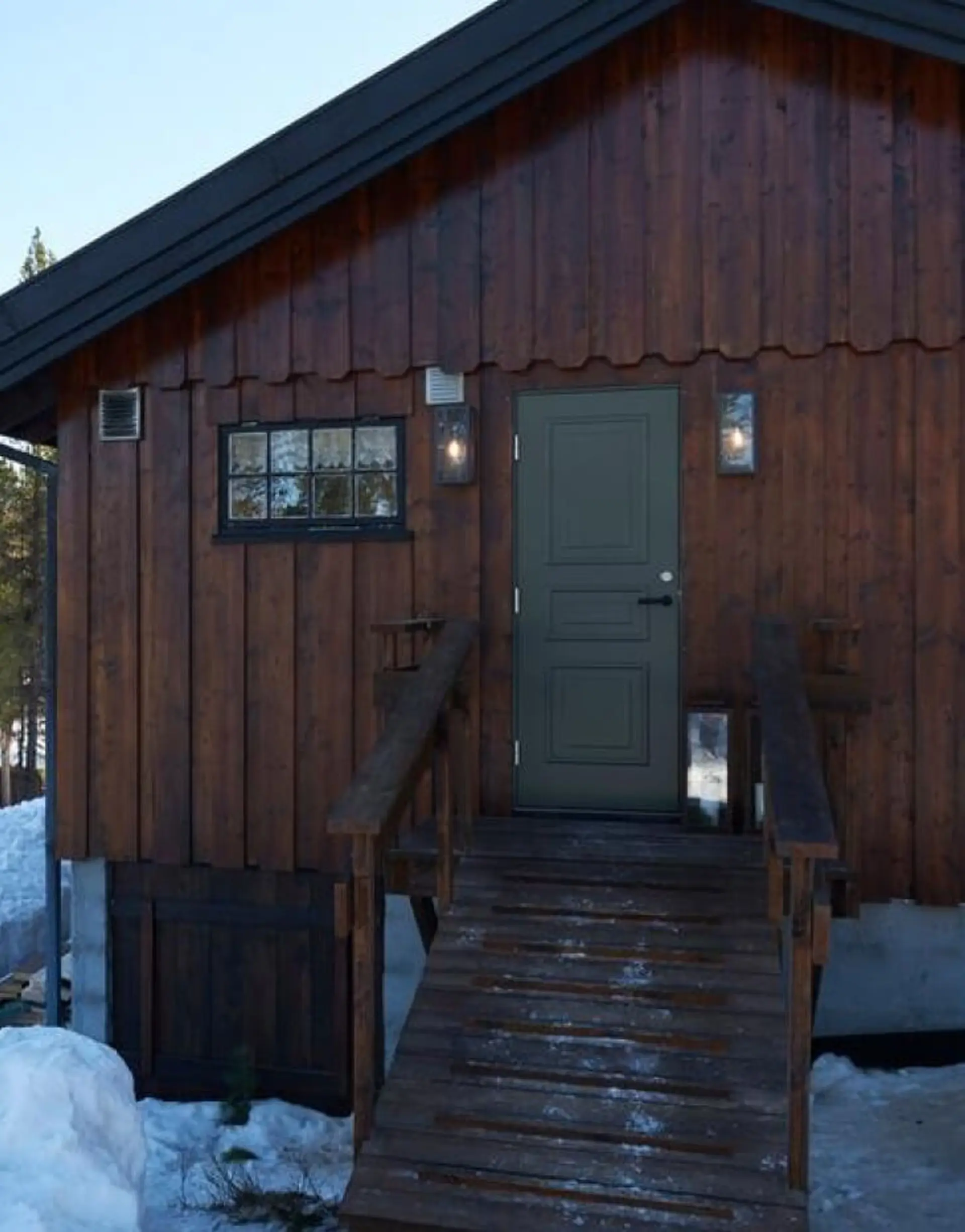Brun trehytte med trapp opp til grønn ytterdør.