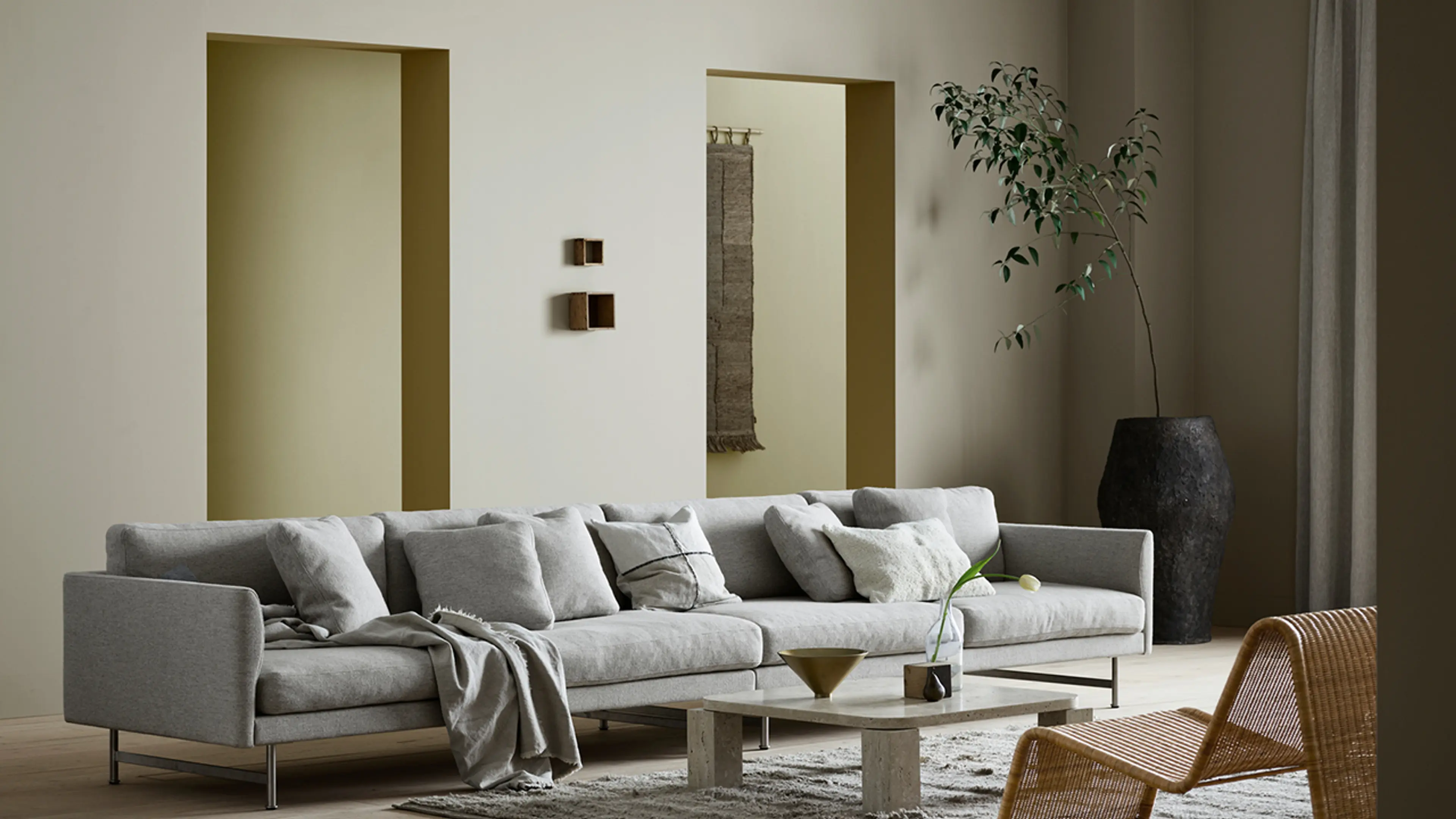Stueinteriør med stor sofa og nøytrale farger i beige, dus gul og grå på veggene.