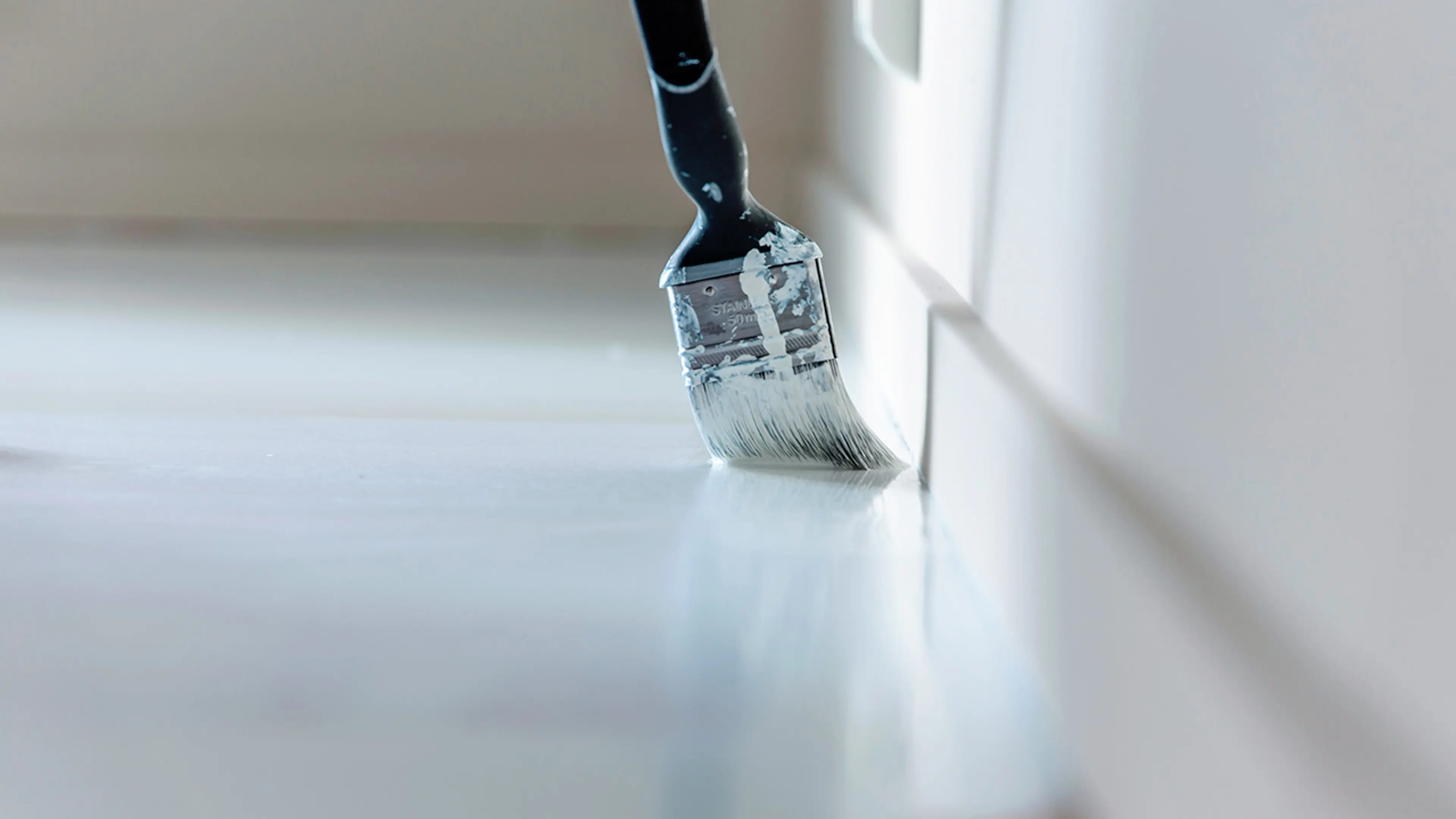 Pensel som maler inntil veggen med gulvmaling.