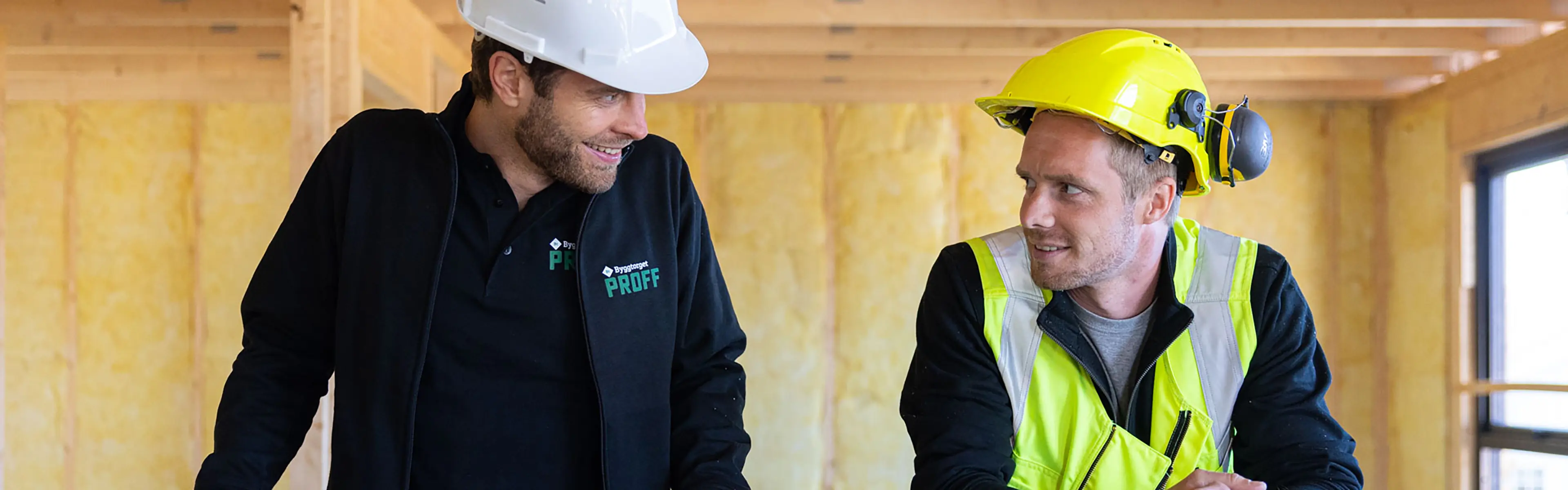to håndverkere står inne på en byggeplass og smiler til hverandre