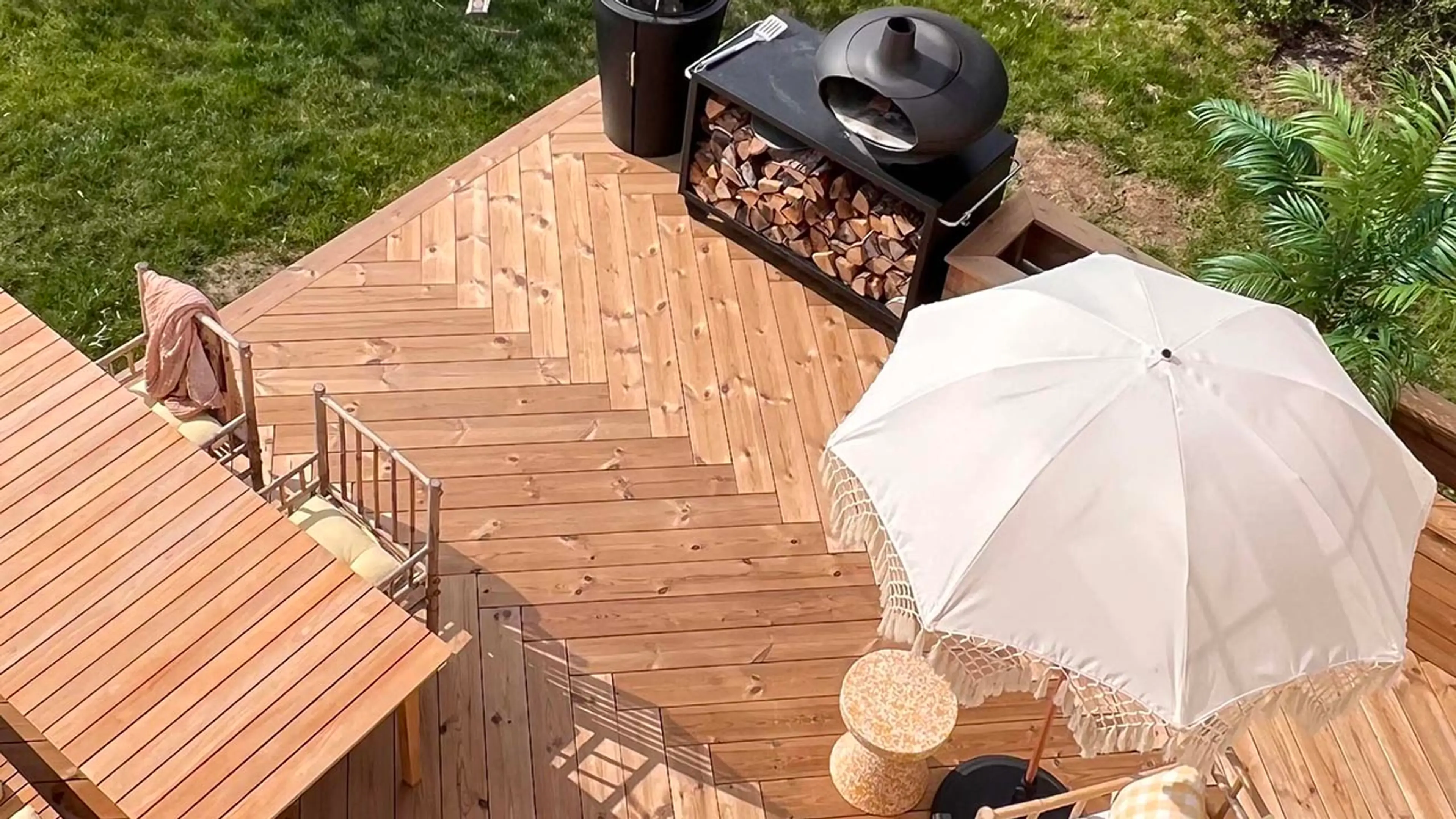 Terrasse i termofuru med fiskebeinsmønster med spisebord og parasoll sett i fugleperspektiv.