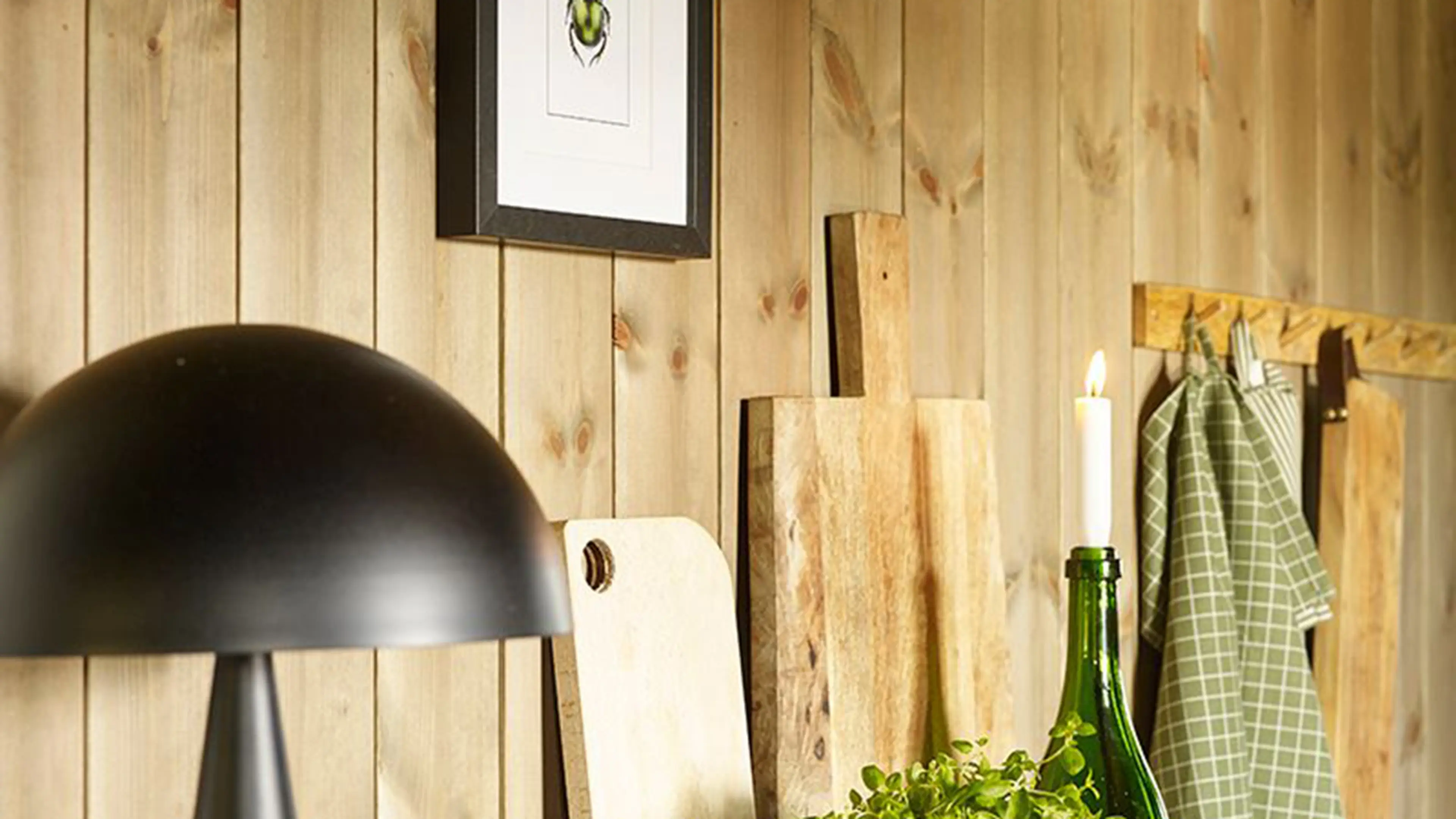Nærbilde av kjøkkenhylle med lampe, urter og skjærefjøl på hytte. Beiset panel på veggen.