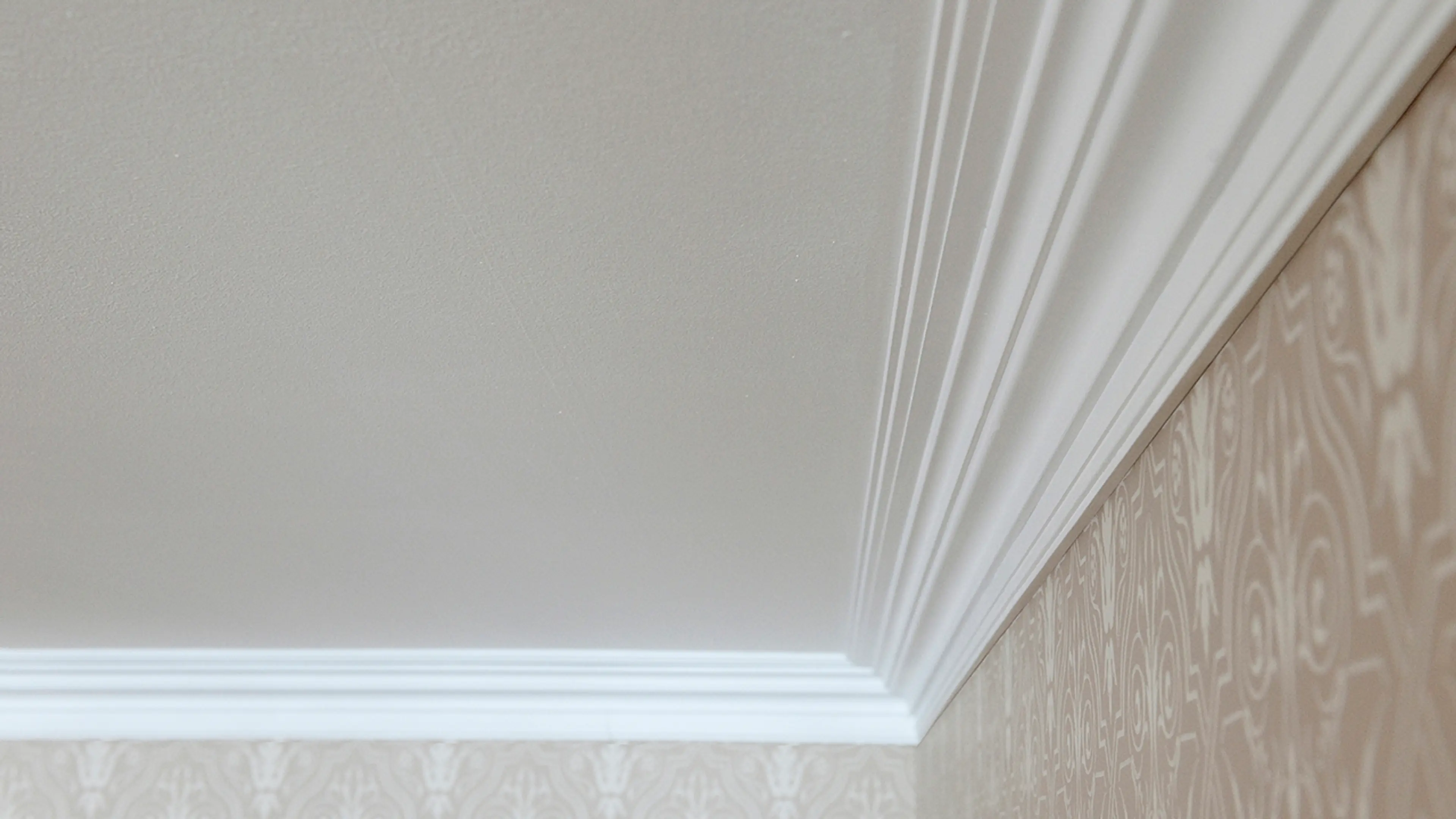 Profilerte lister i taket til vegg med mønstret tapet.