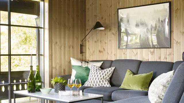 Stue med grå sofa og hvitt marmorbord i hytte med furupanel på veggene.