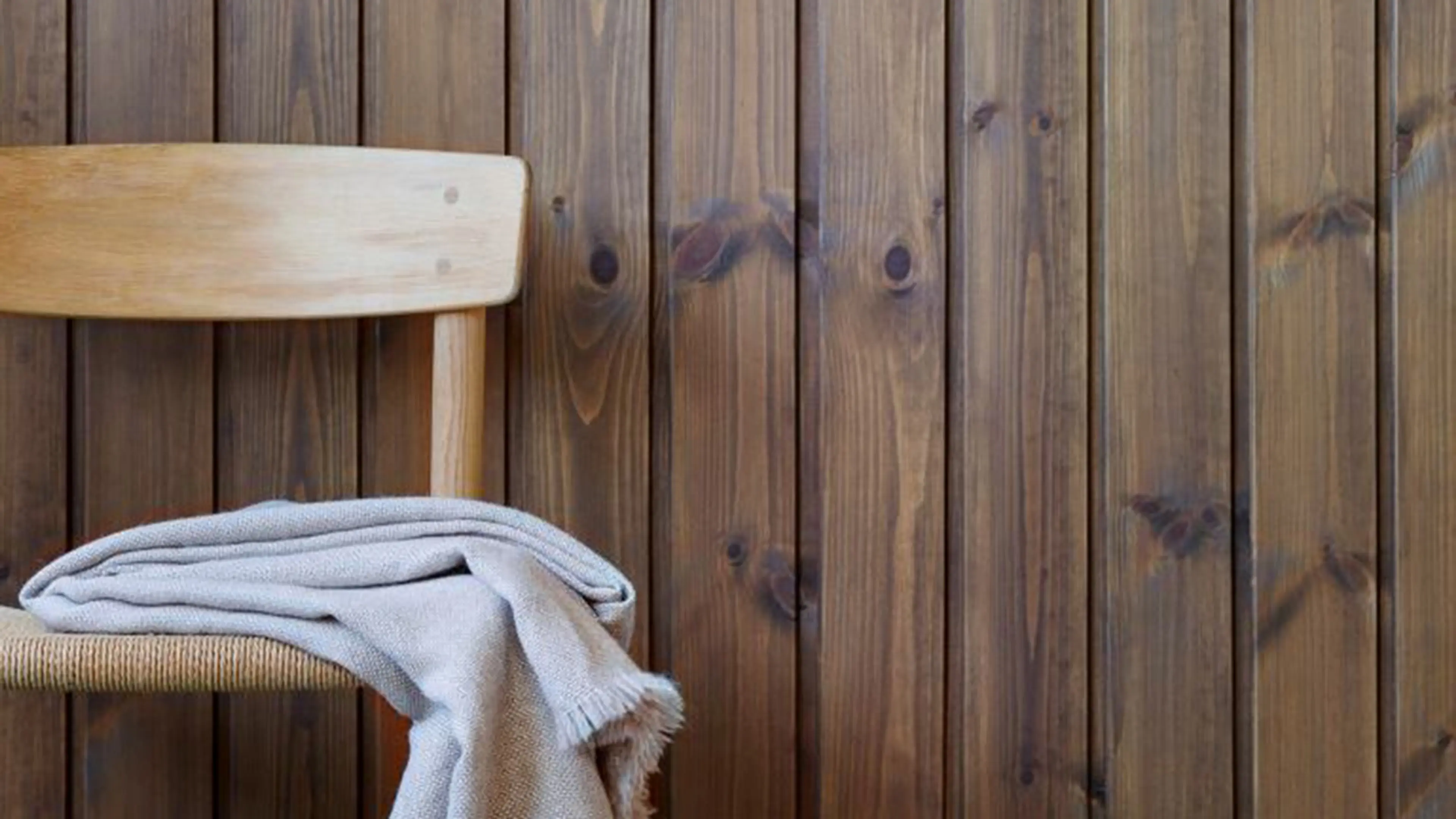 Lys eikestol med pledd på foran veggpanel med brun panellakk fra Jotun i fargen 90024 Dyp Brun.