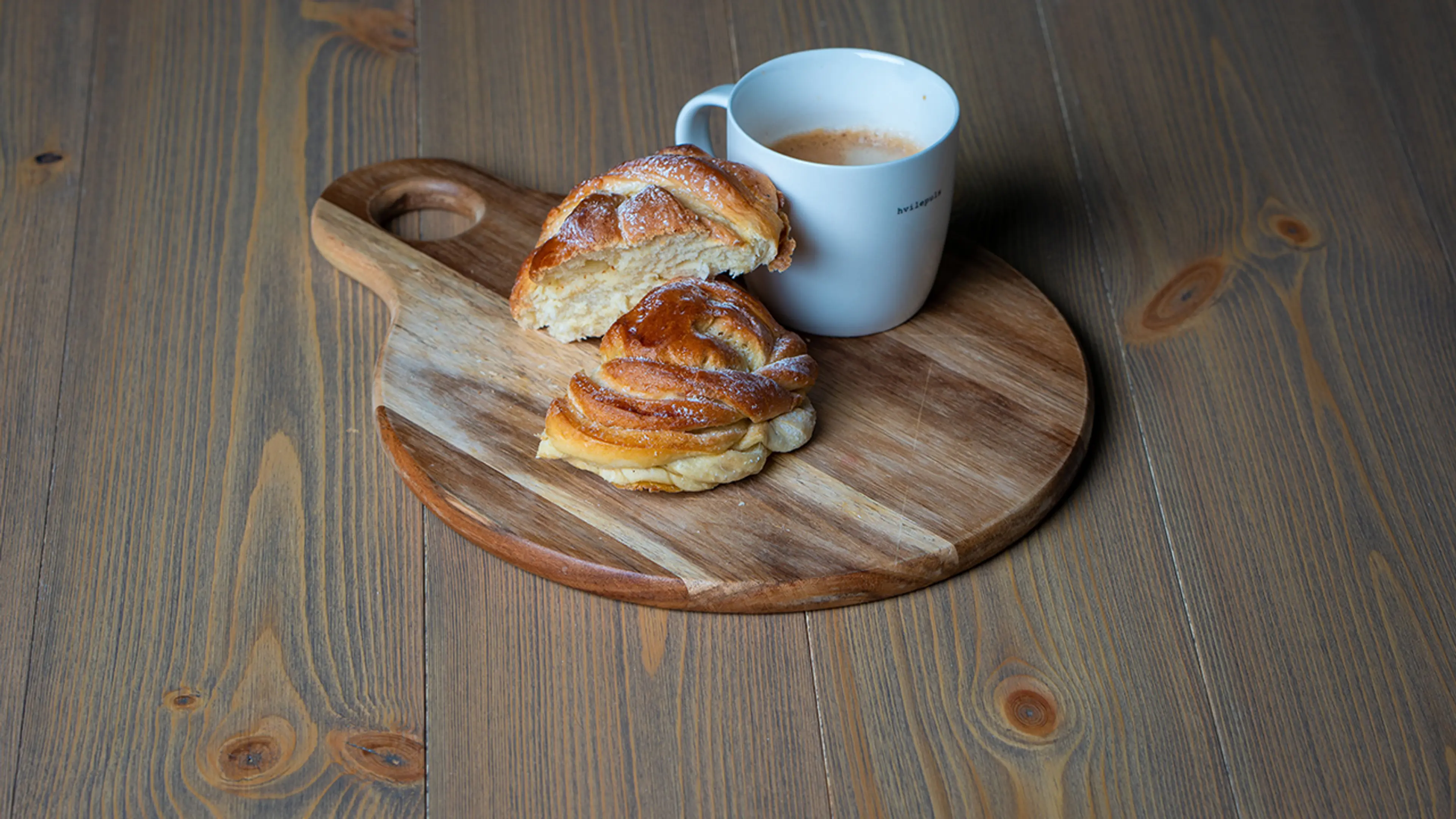 Nærbilde av oljet heltregulv i furu med skjærebrett, kanelbolle og kaffekopp.