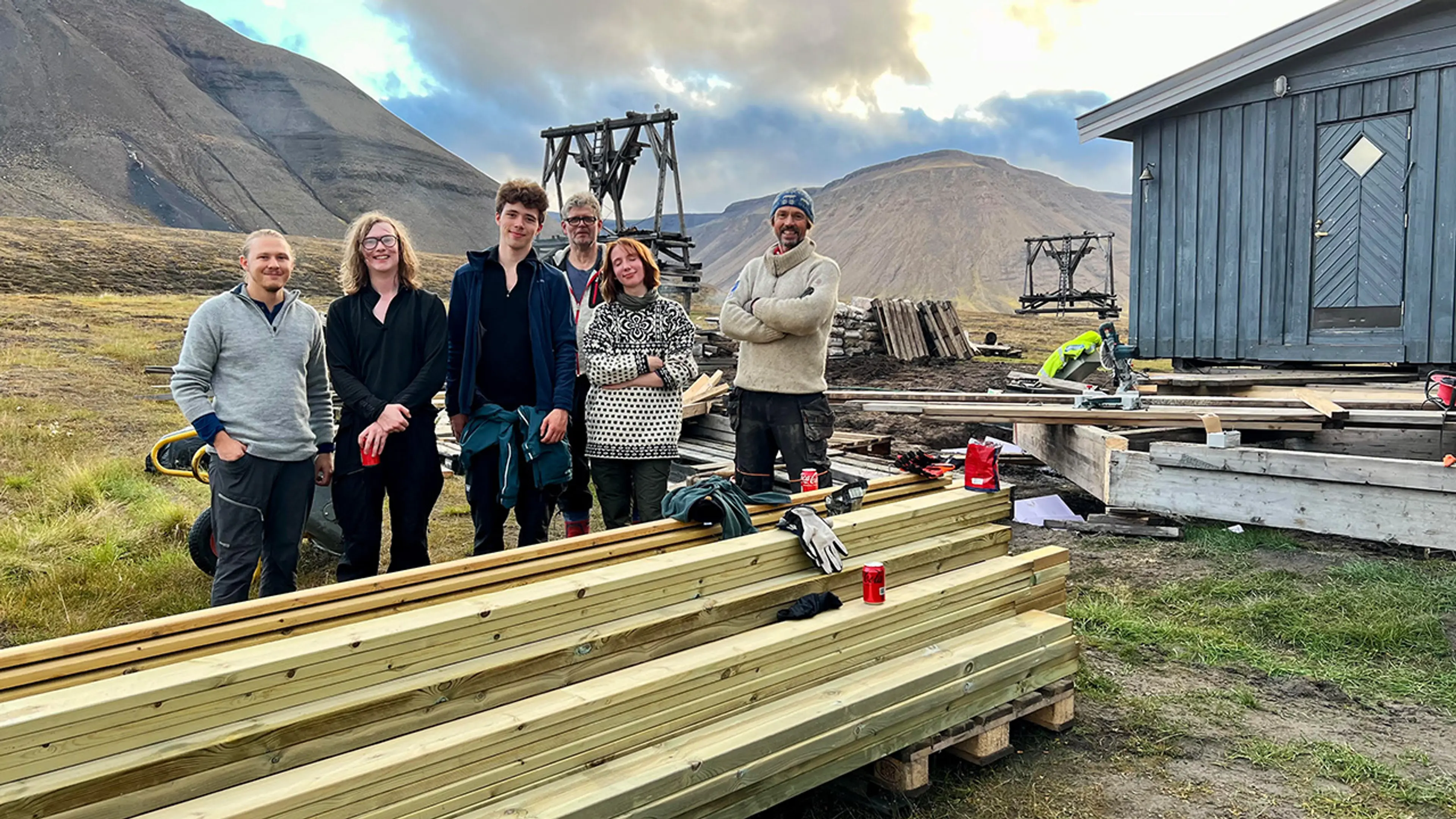 6 personer som står og smiler bak en stabel med planker på Svalbard.