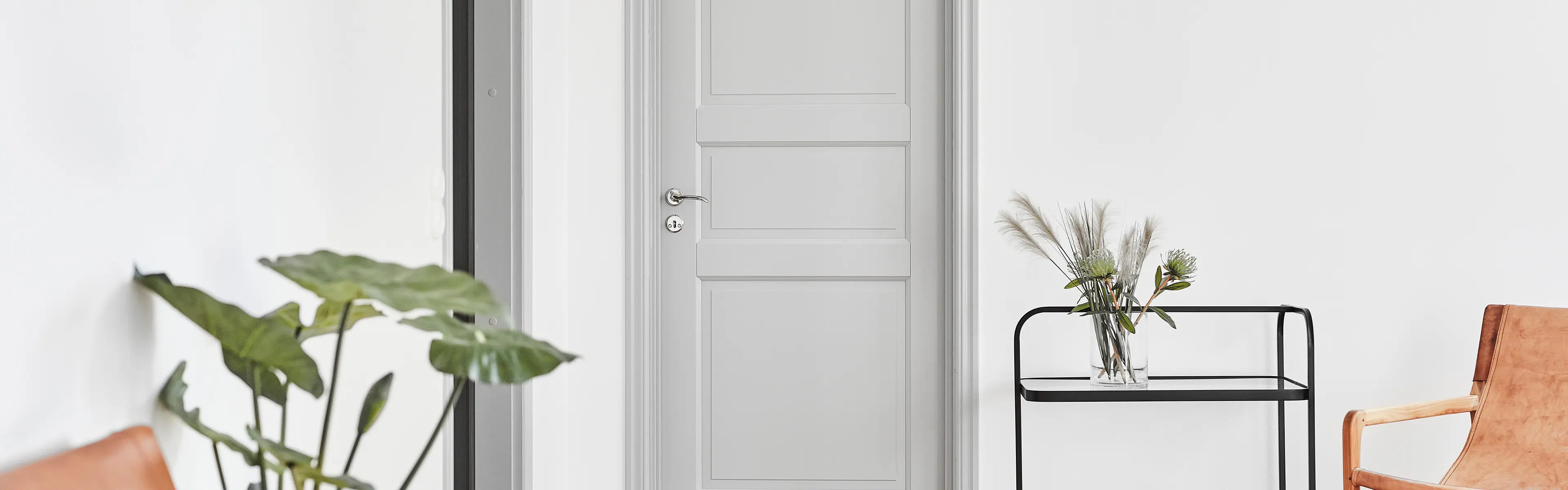 Lys grå innerdør med profil i stue med skinnstoler, grønne planter og trillebord.