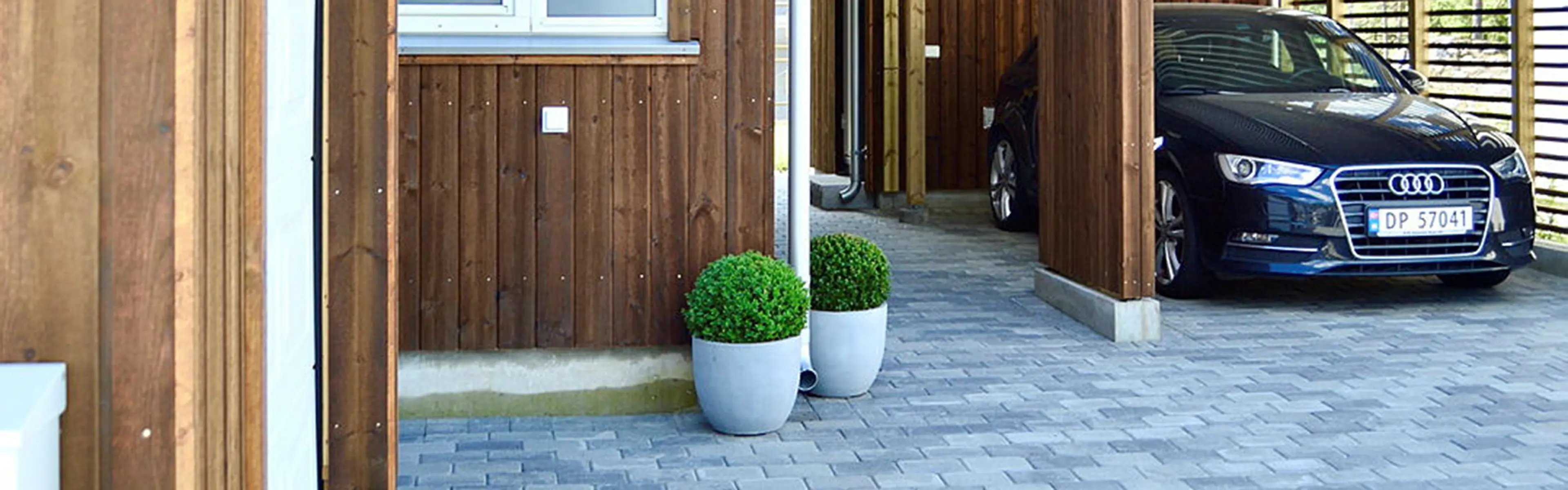 Belegningsstein på gårdsplass og en bil parkert i carport.