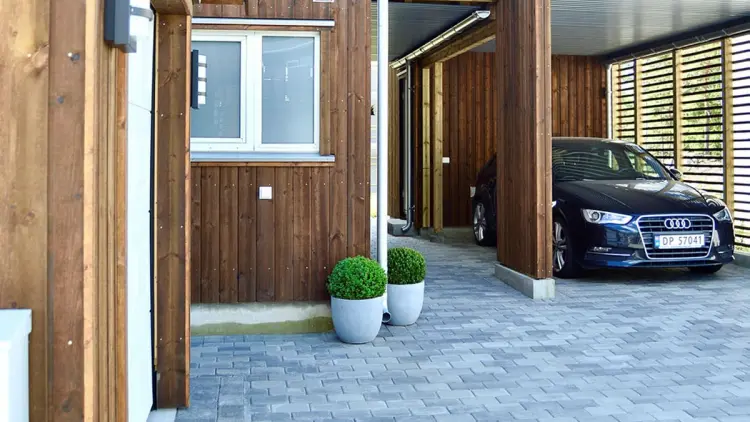 Gårdsplass med belegningsstein og en bil parkert i carport.