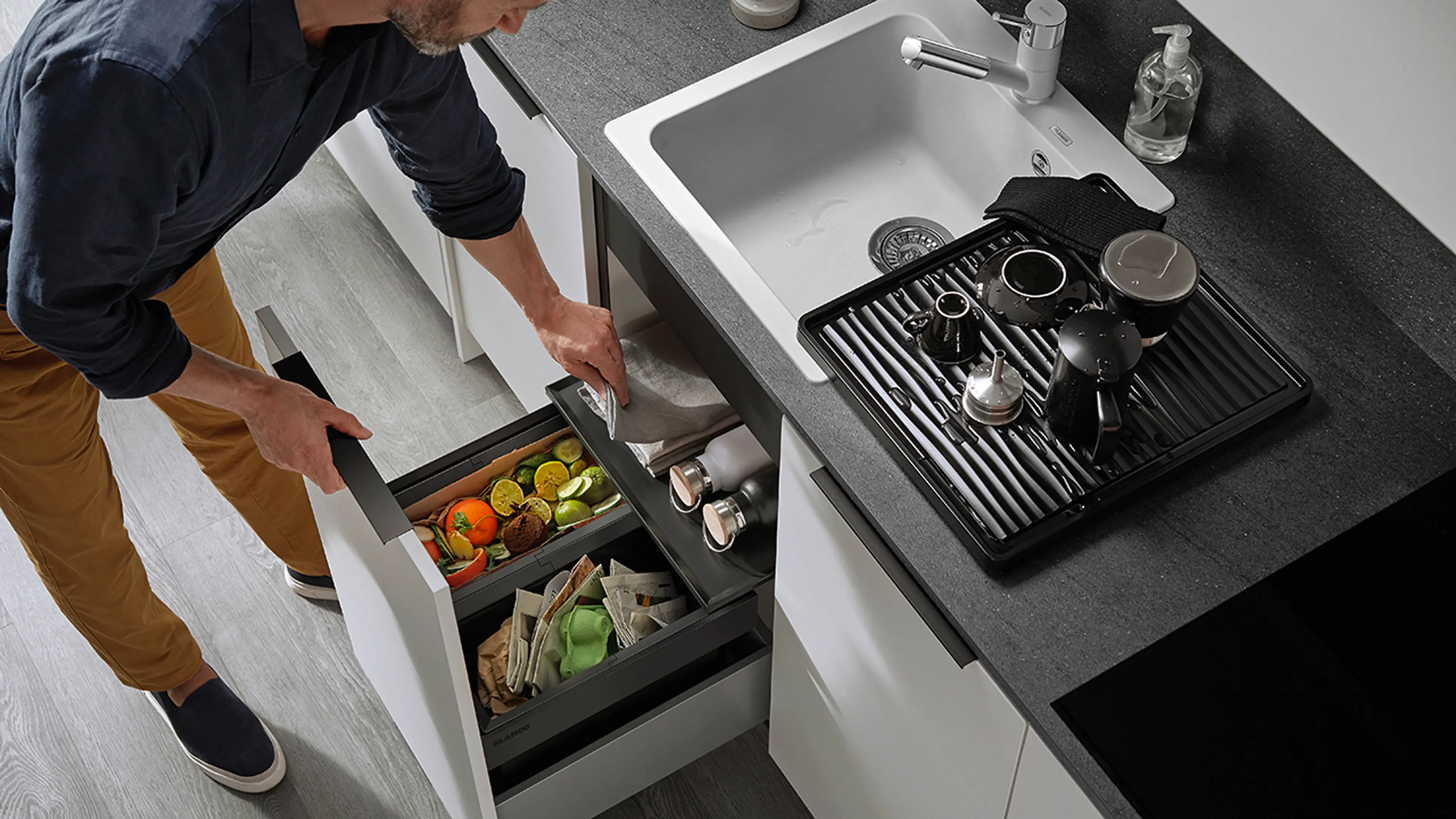 Mann på kjøkken med søppelsortering i skuff under vasken.