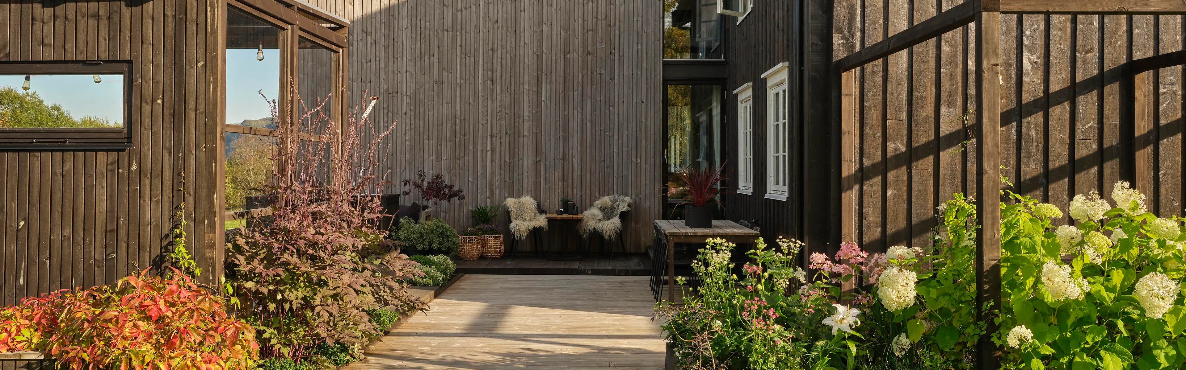 Uteplass og terrasse med pergola og varme farger på terrassebord som er en av årets hagetrender.