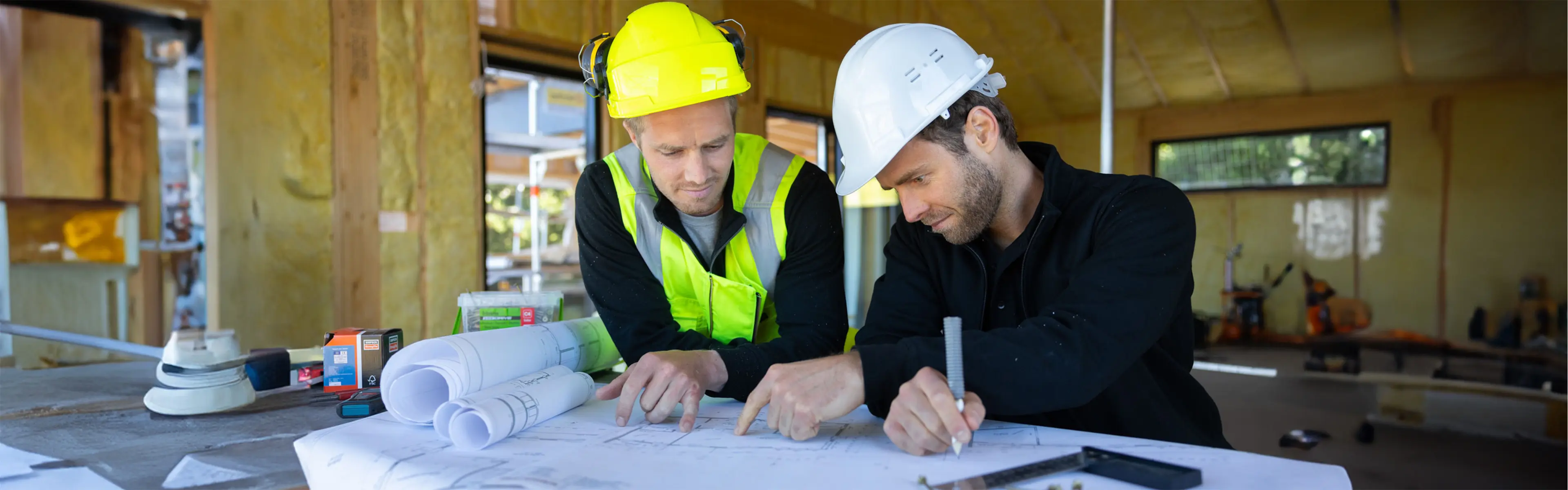 To menn som ser på plantegninger i et hus under bygging.