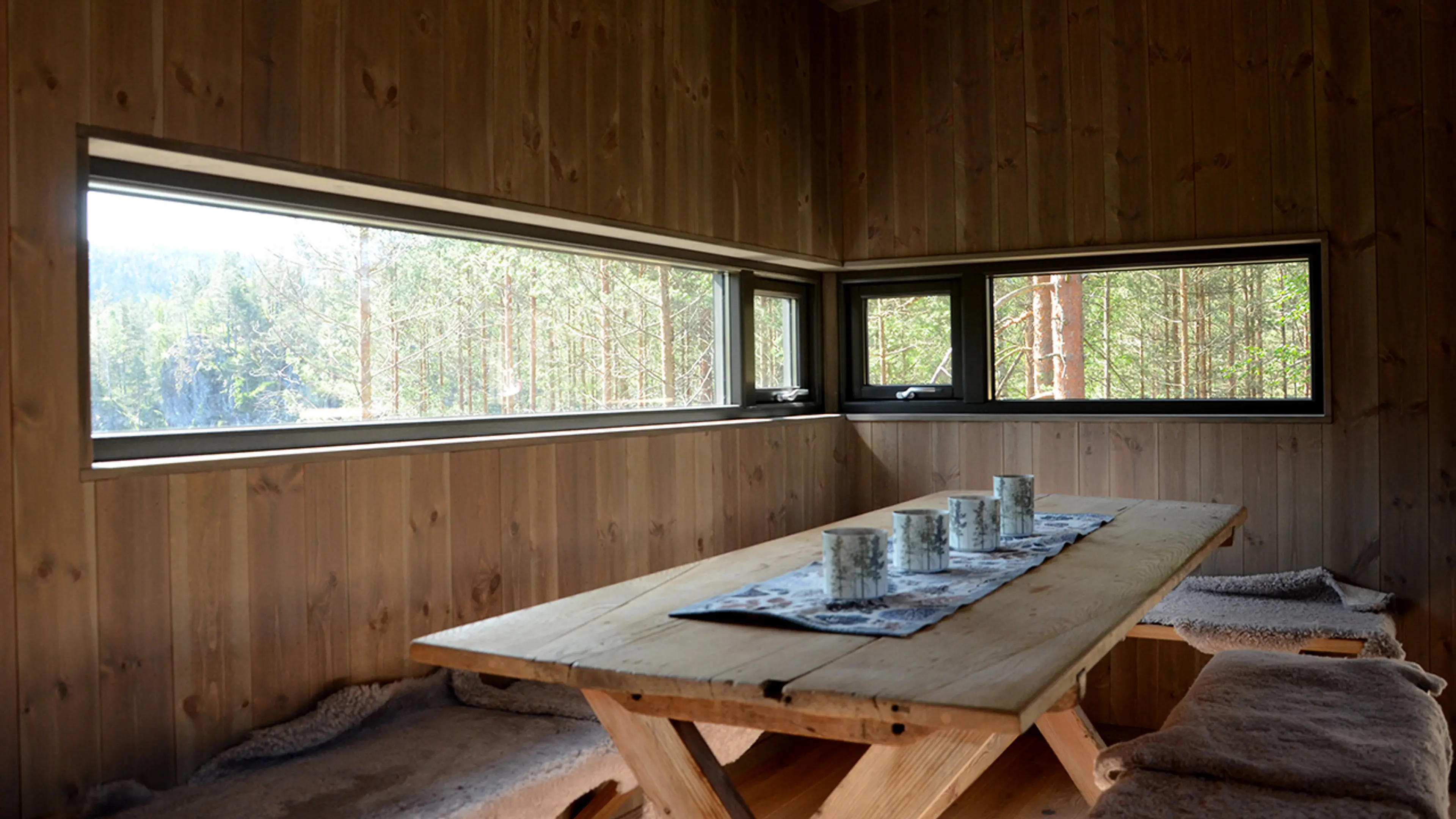 Spisestue i hytte med panelvegger og sorte smale vinduer.