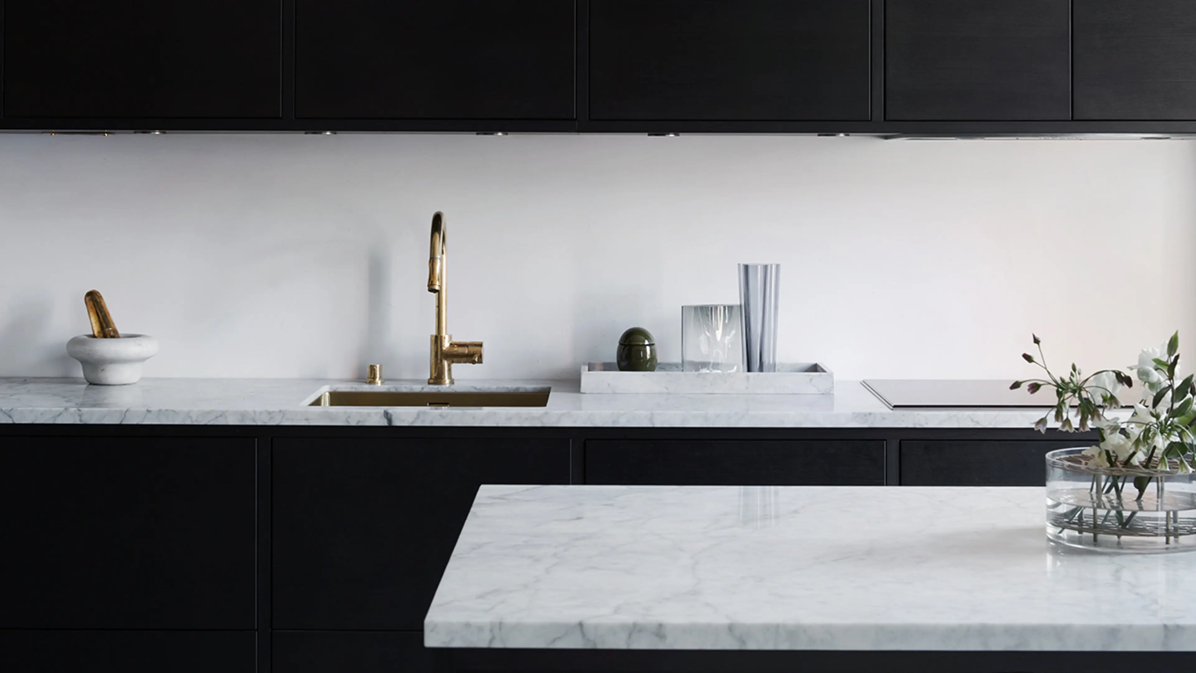 Benkeplate i marmor i svart kjøkken med messing servant og blandebatteri.