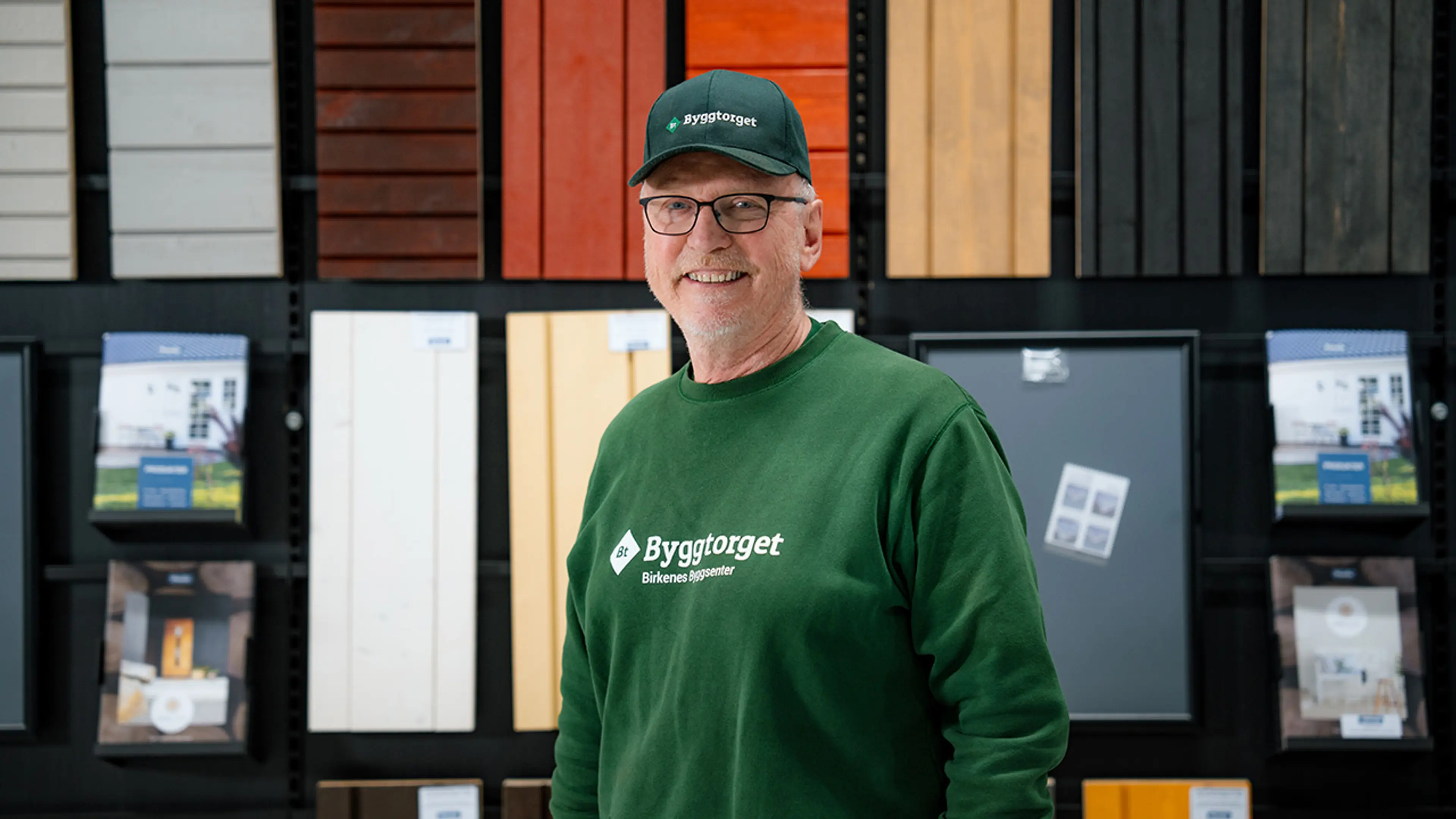 Byggtorget-ansatt i byggevarehus foran en vegg med kledning.