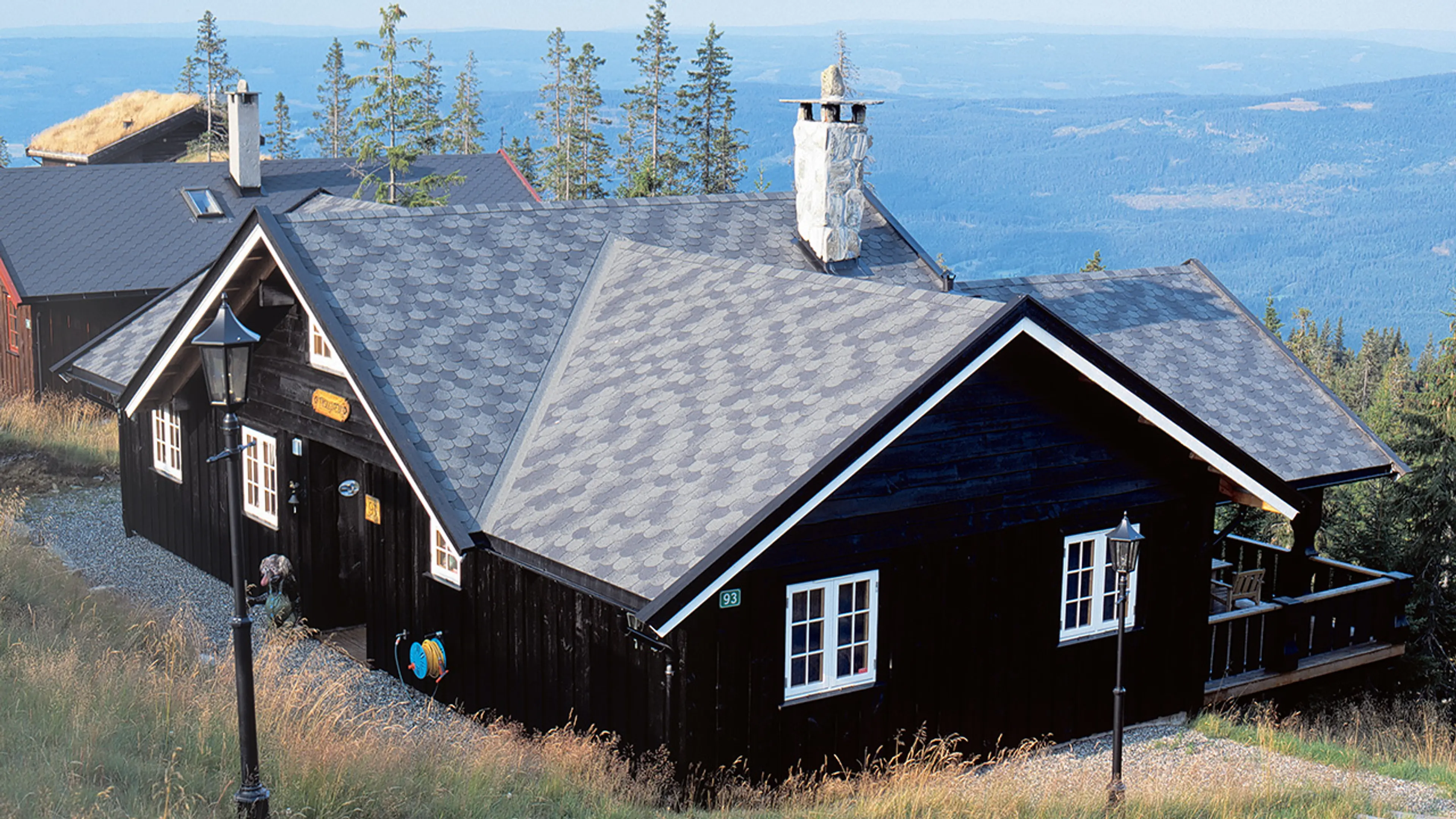 Svart hytte med grå Isola takshingel på taket.