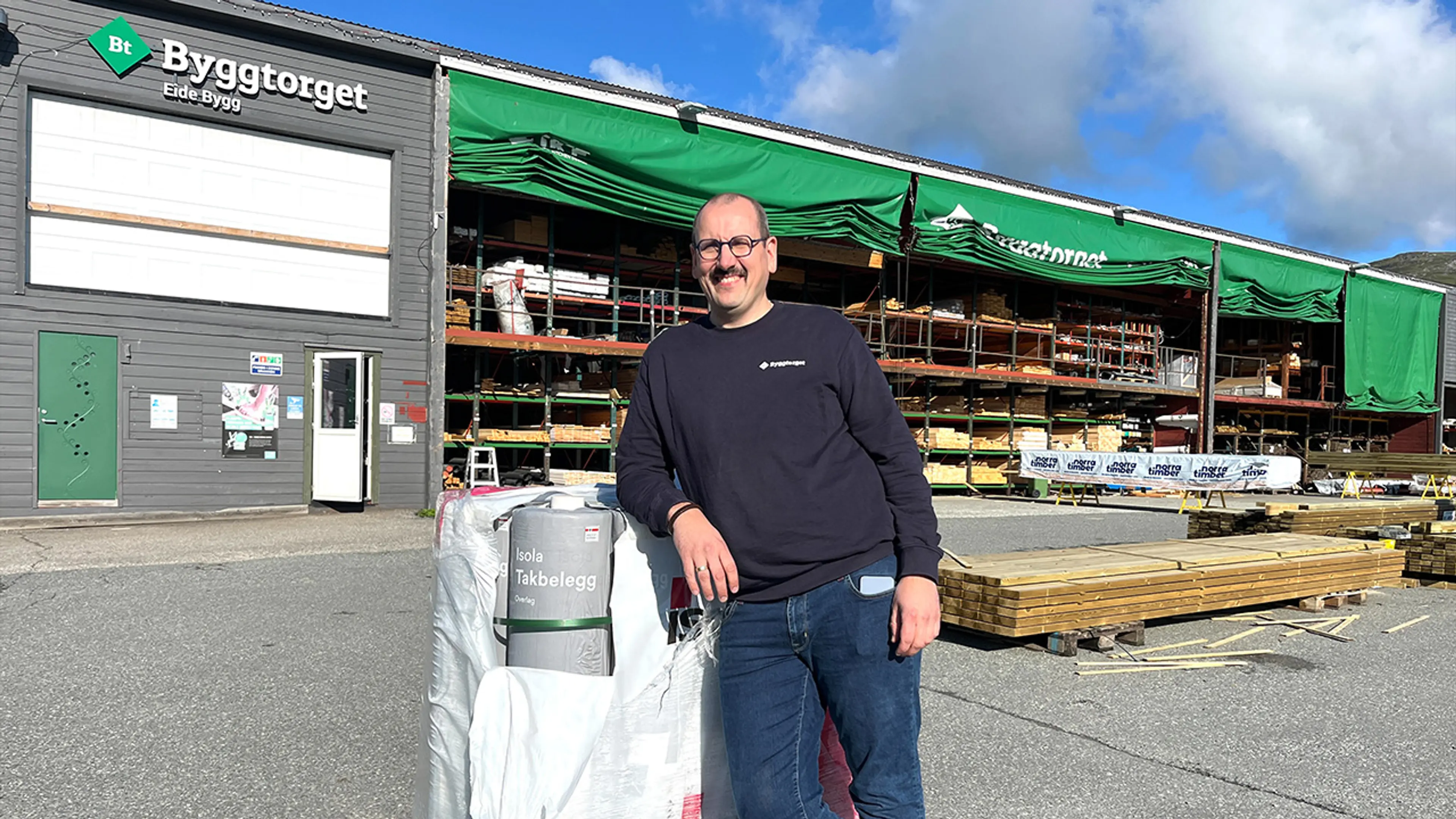 Byggtorget ansatt som smiler til kamera foran byggevarehuset, Byggtorget Eide Bygg