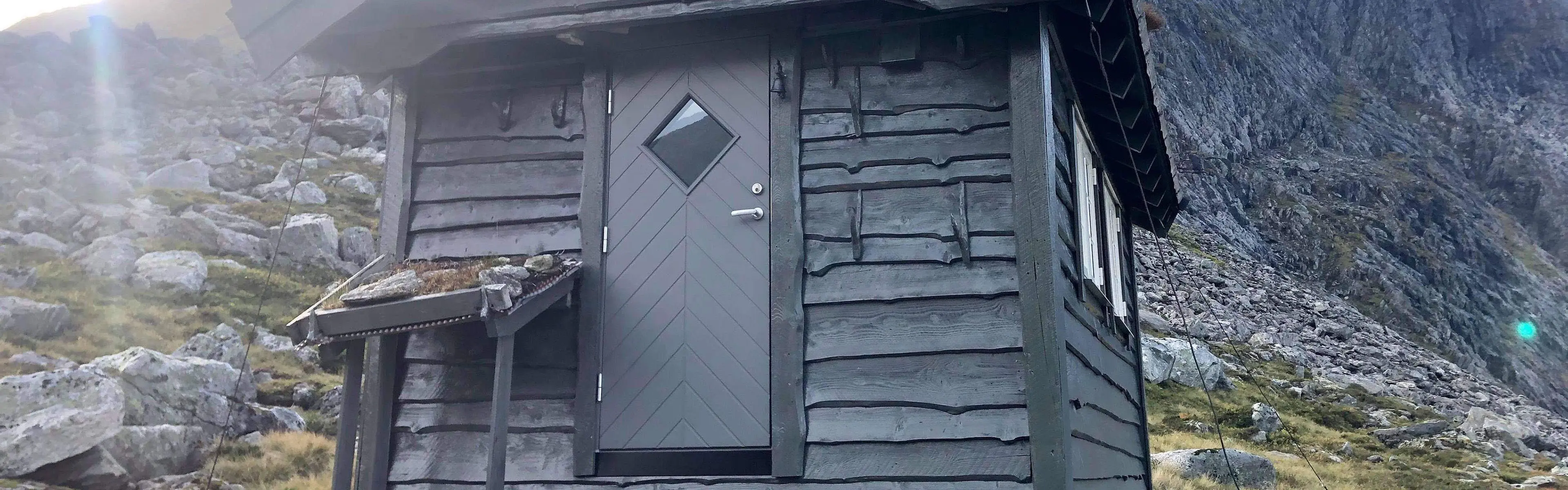 Grå ytterdør på en liten hytte i fjellheimen.