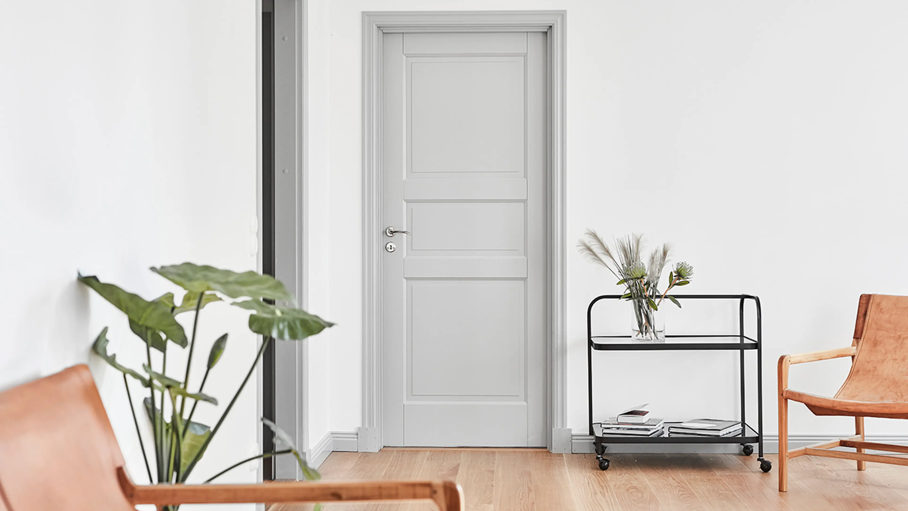 Lys grå innerdør med profil i stue med skinnstoler, grønne planter og trillebord.