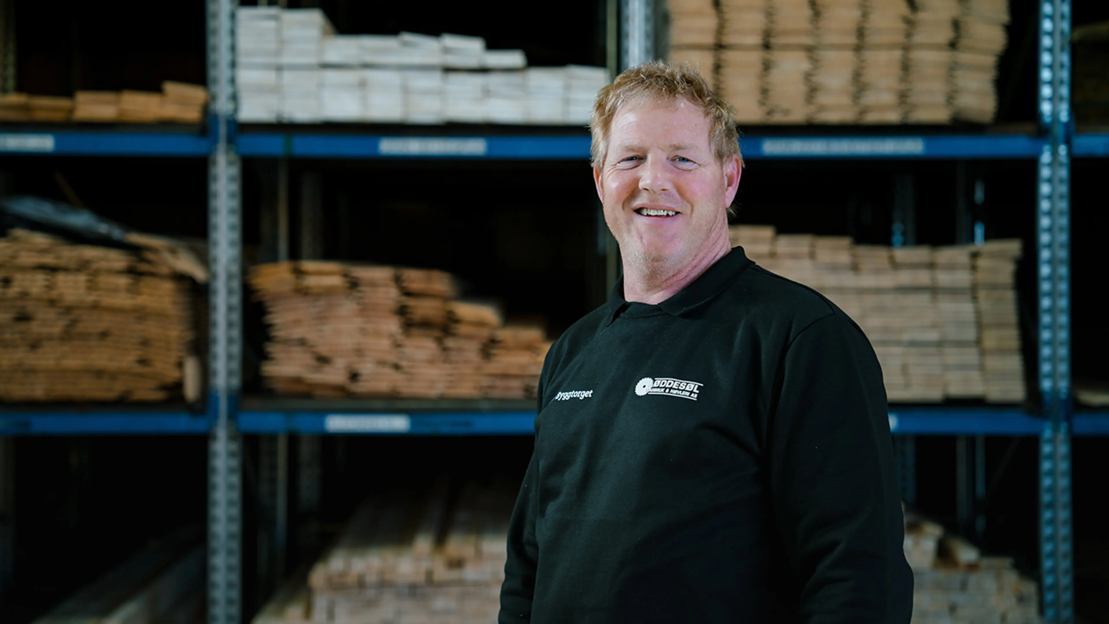 Byggtorget-ansatt i byggevarehus foran hylle med trevirke.