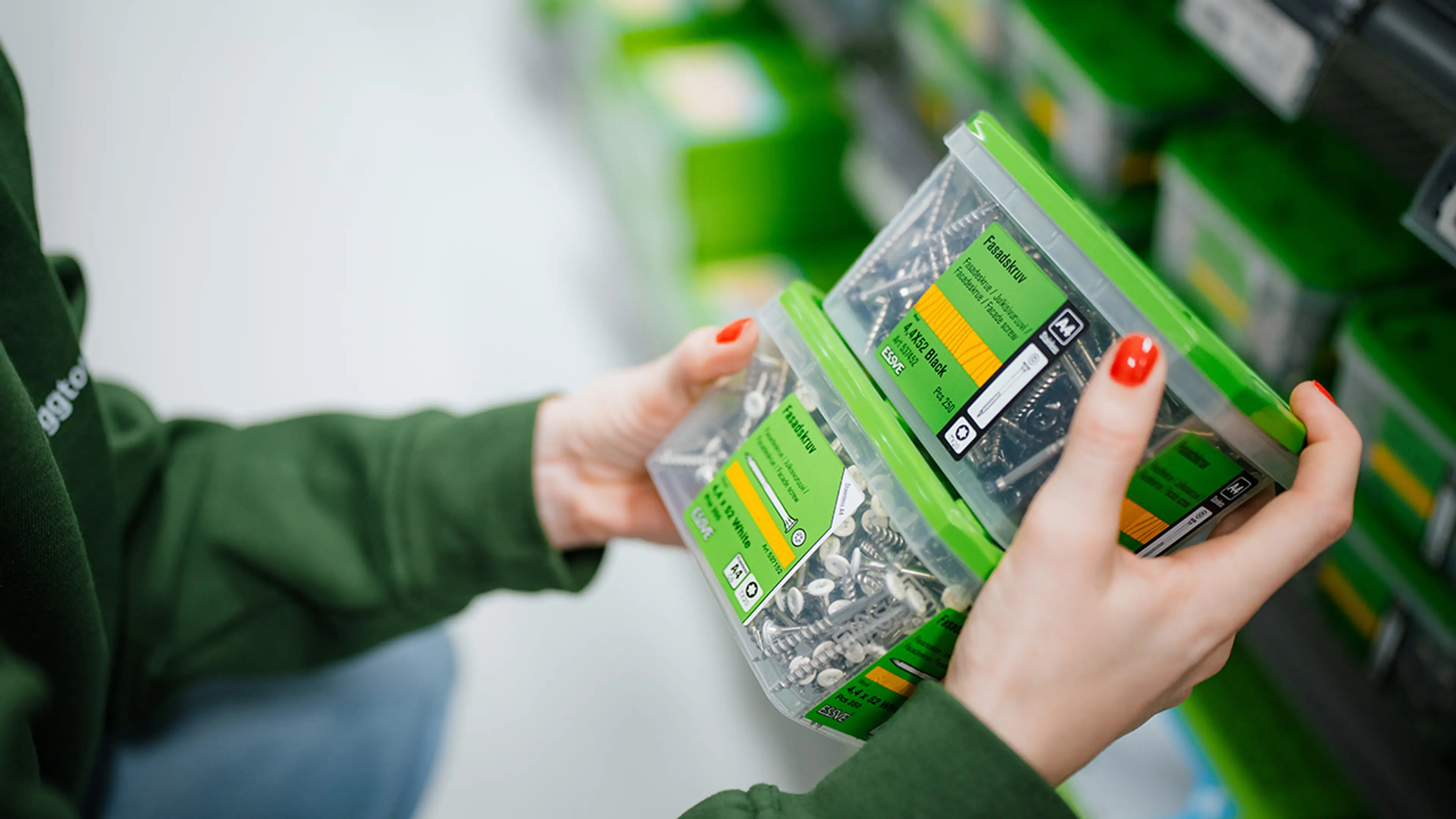 Hender som holder to bokser med fasadeskruer med skuehoder i svart og hvit.