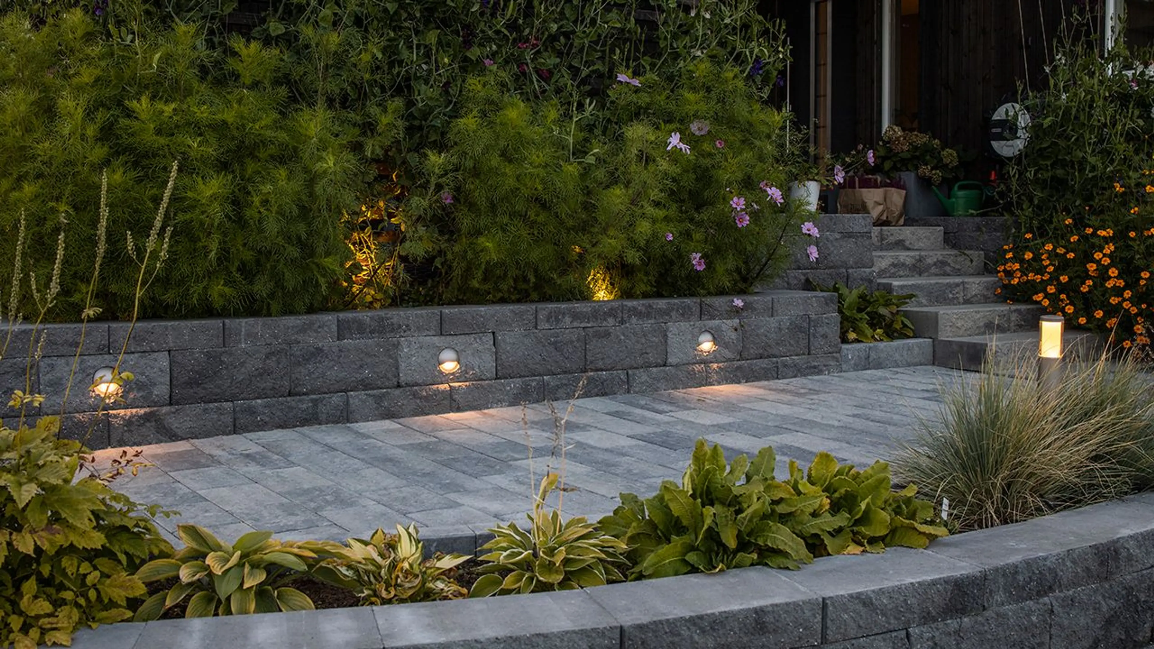 Norsk hage med utebelysning i mur som er blomsterbed.
