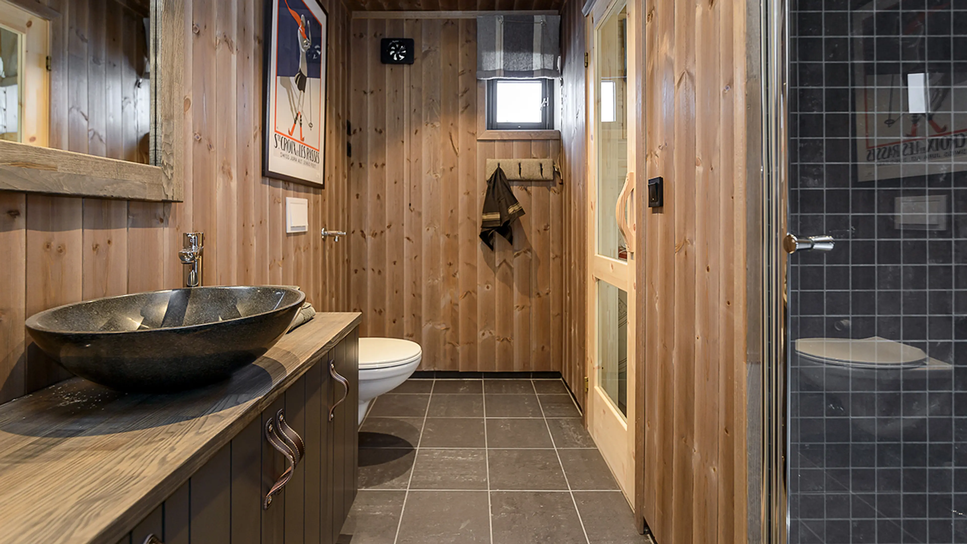 Lite hyttebad med trepanel og baderomsinnredning i treverk med skinnhåndtak.