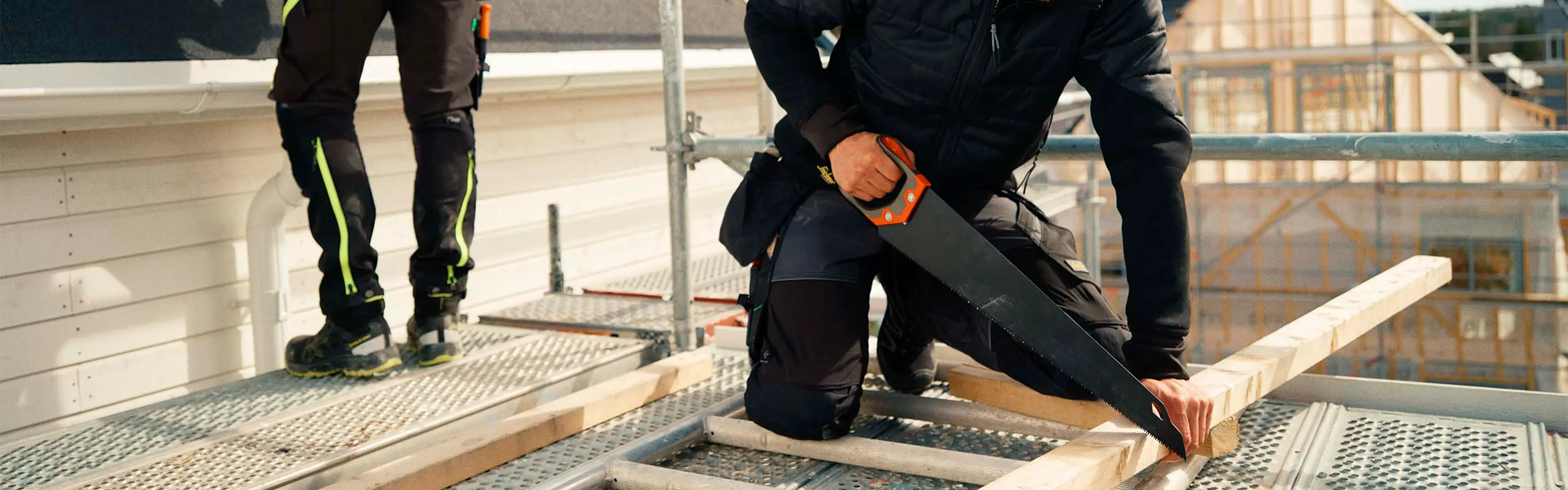 Håndverkere som arbeider med tak og sager på stillas med arbeidsklær.