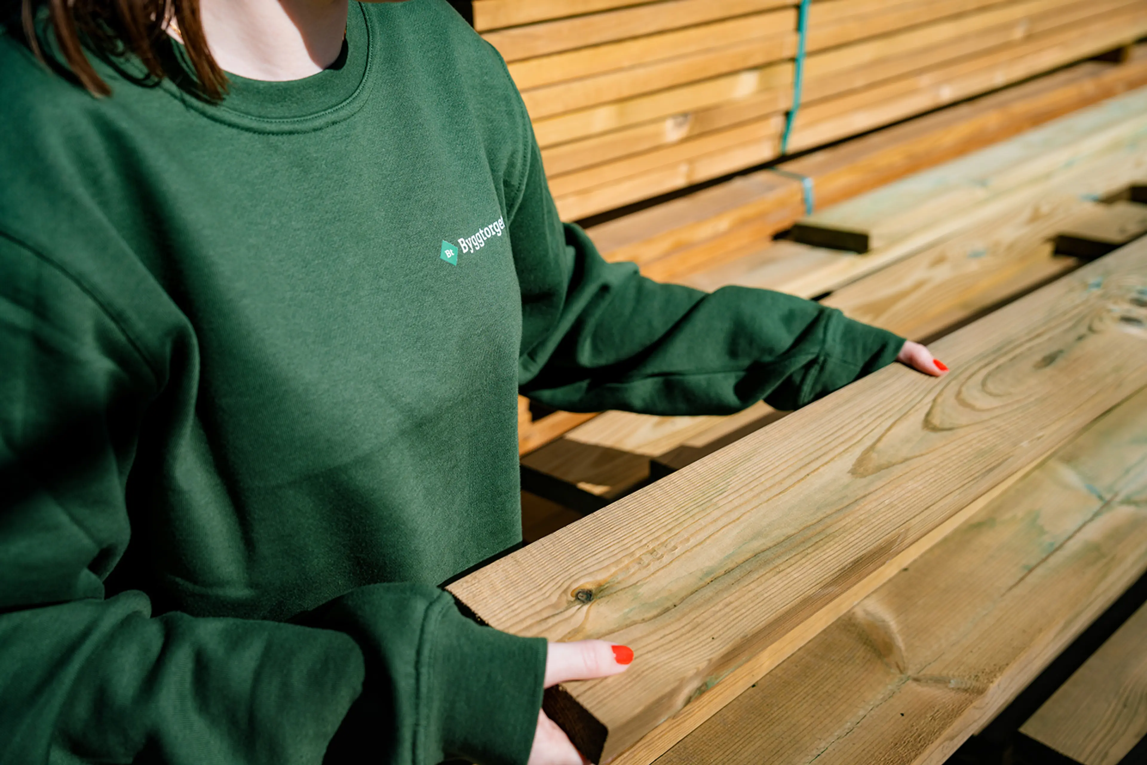 dame i Byggtorget-genser viser frem trykkimpregnert terrassebord