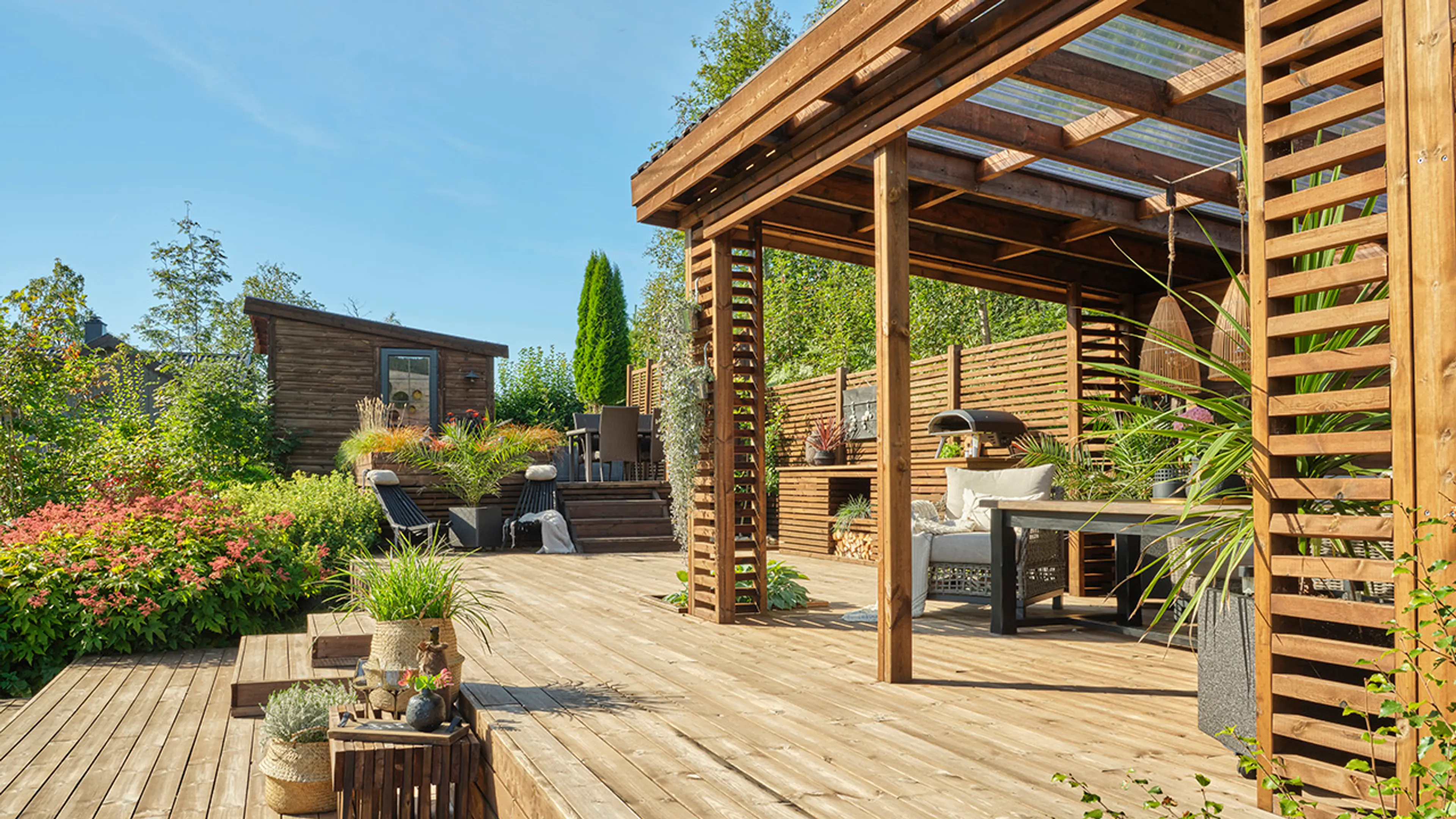 Stor pergola med spiseplass på terrasse med ulike nivåer.