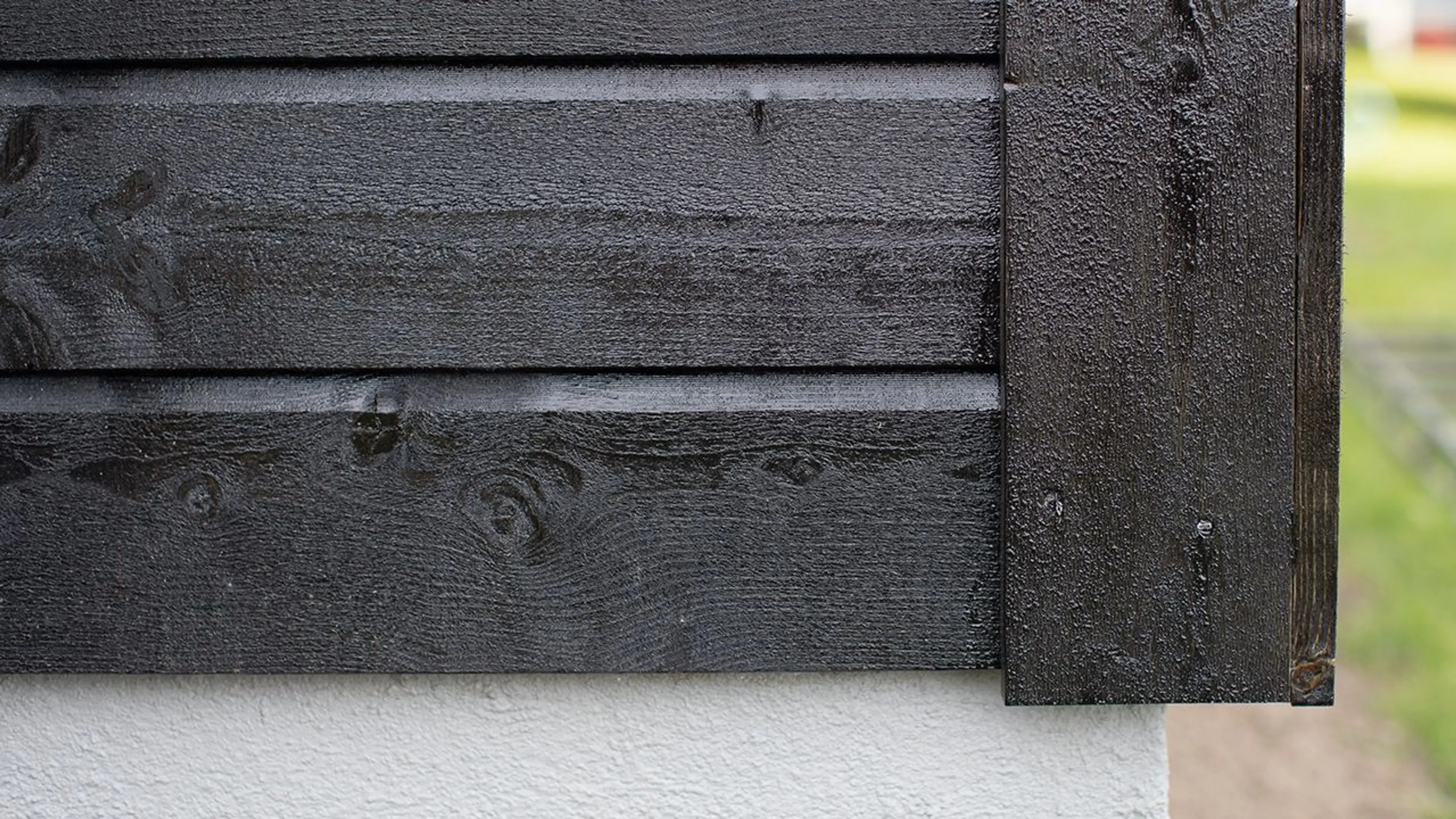 Nærbilde av sort dobbelfals kledning på hus med hvit grunnmur.