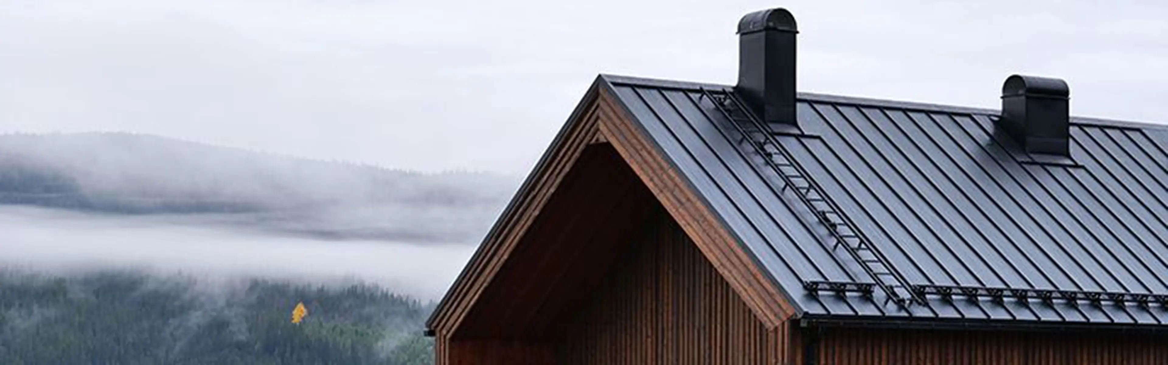 Toppen av brunt trehus med svarte takplater aluminium på taket.