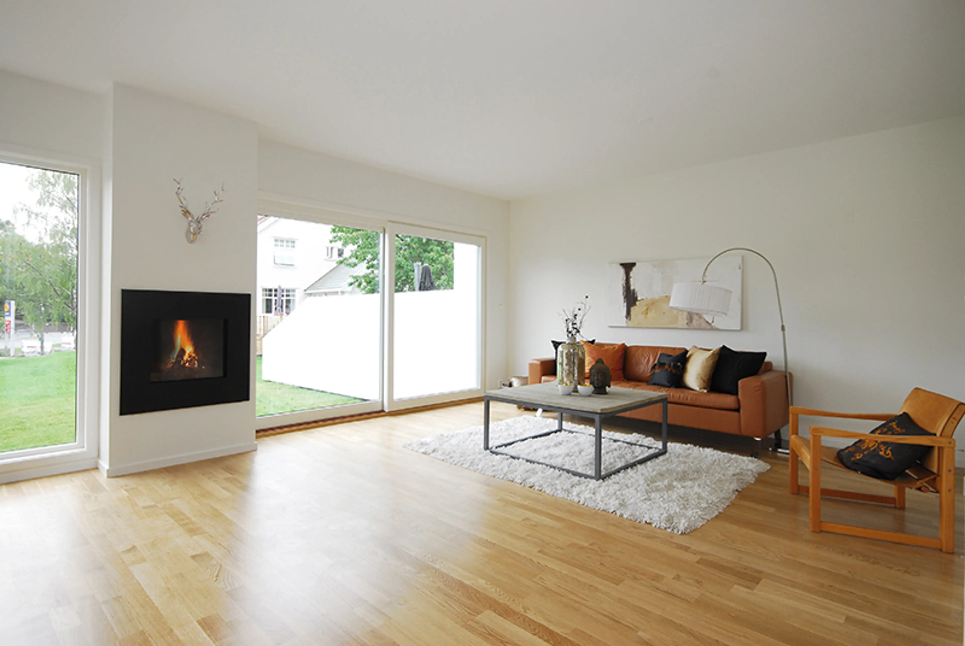 moderne stue med store vinduer mot hagen. Brun skinnsofa og peis i veggen.