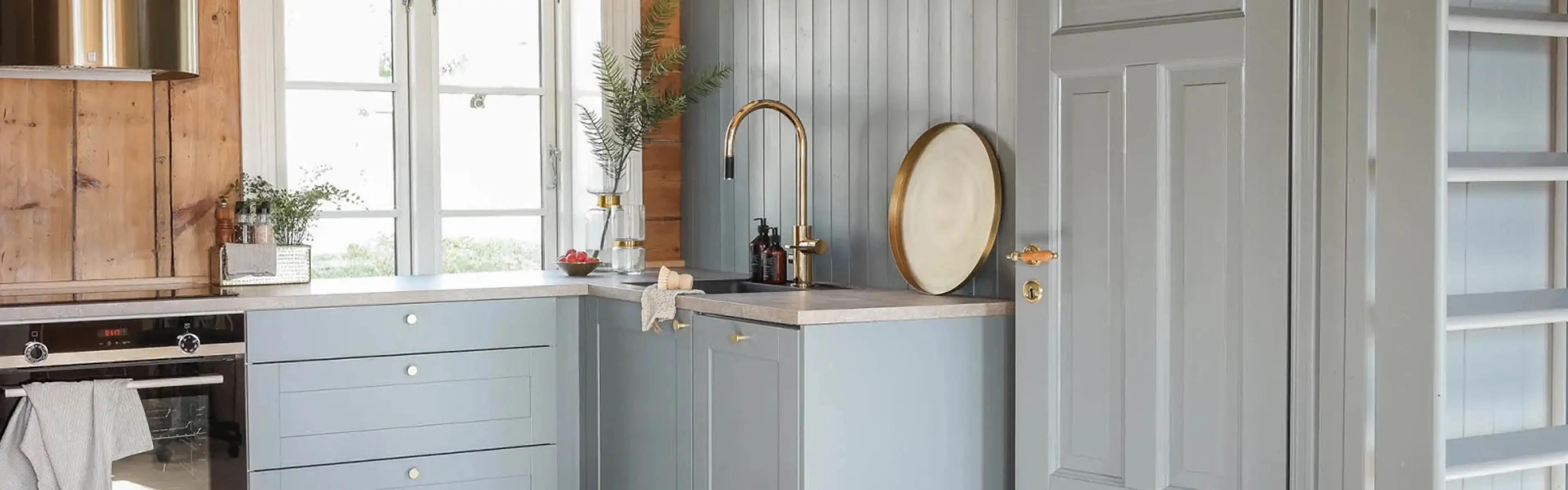 Hyttekjøkken med kjøkkenhette i messing, innebygd stekeovn og fronter malt i fargen 5044 Isblå fra Jotun.